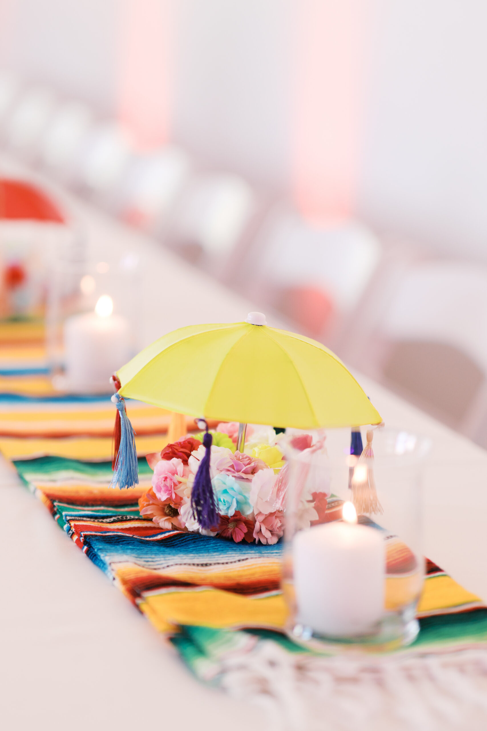 Yellow mini umbrella centerpiece on vibrant striped runner with candlelight.