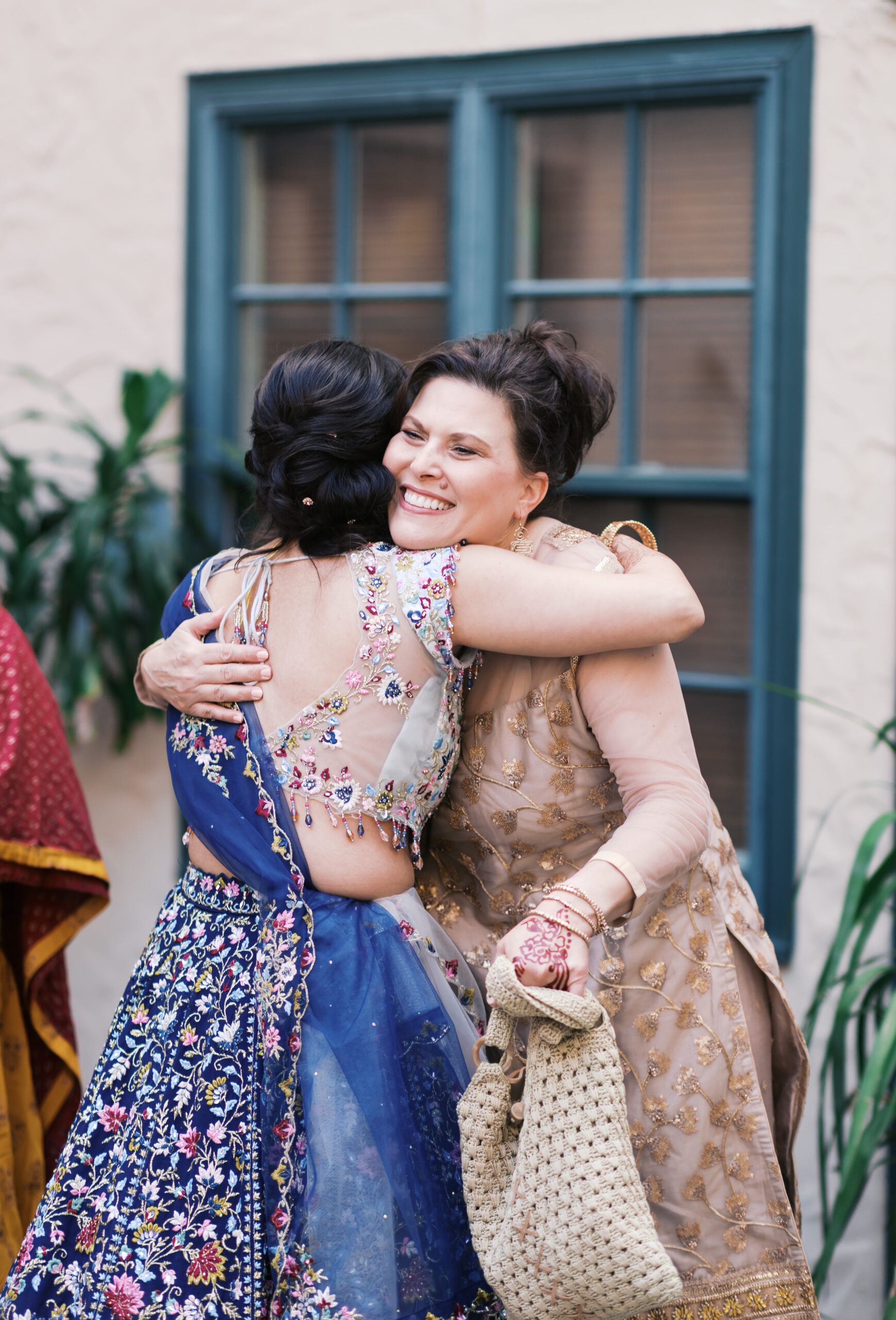 Two guests hugging in embroidered lehengas during Indian wedding celebration.