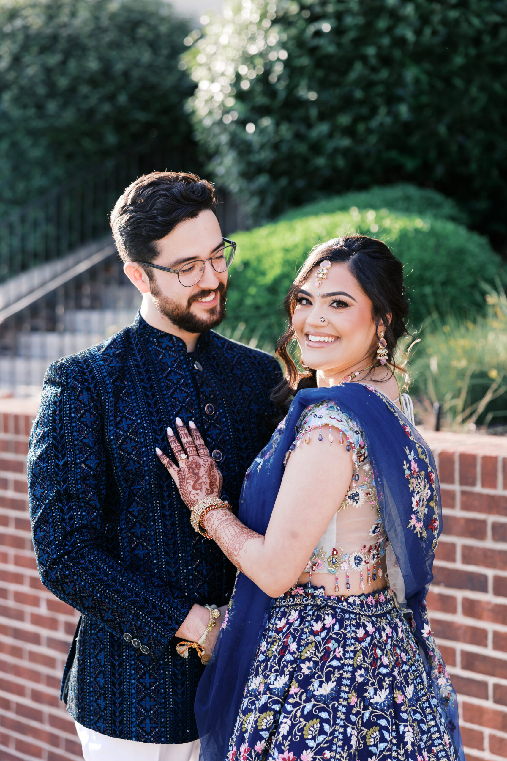 Wedding couple smiling in navy sherwani and floral lehenga.