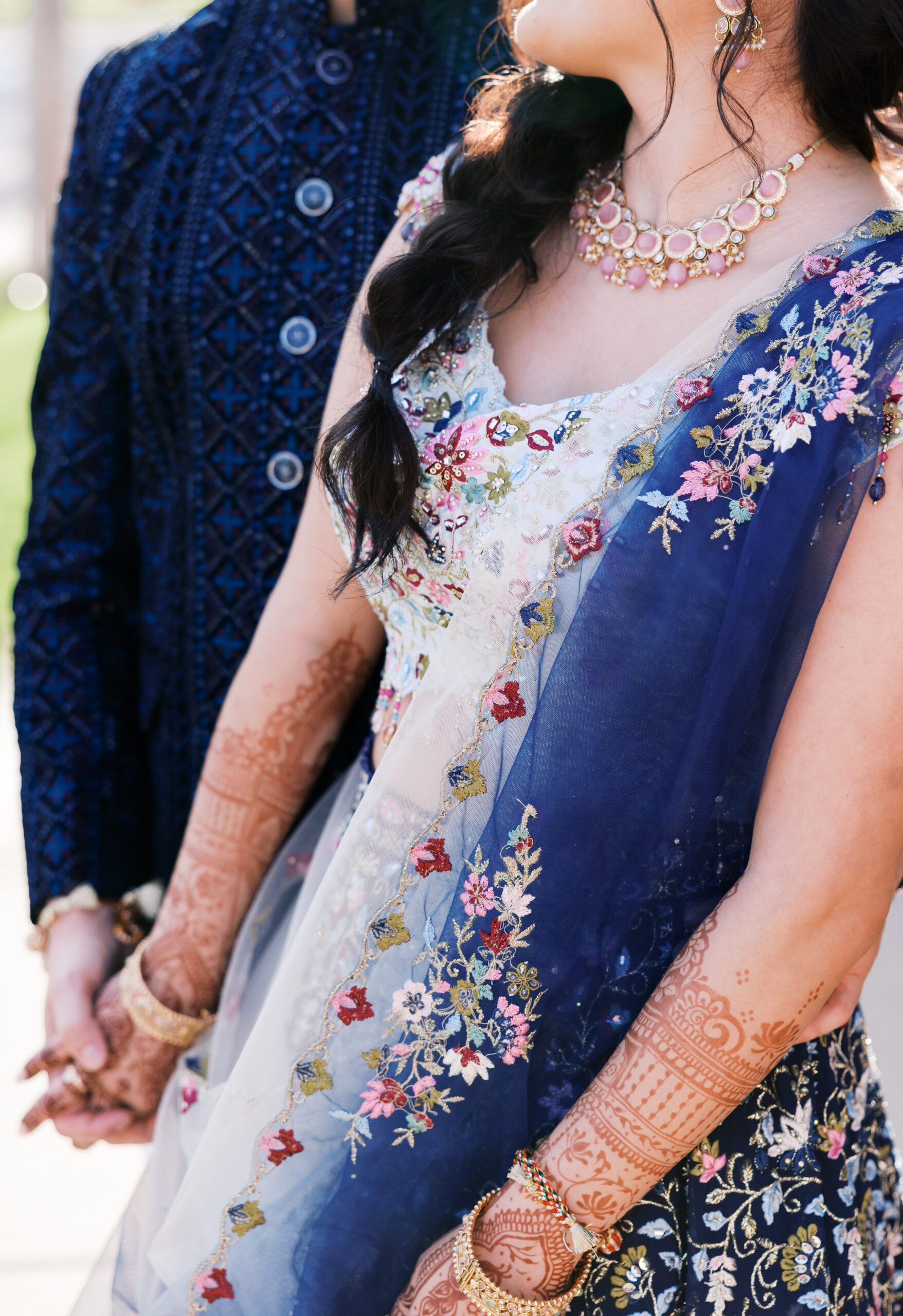 Close-up of bridal lehenga embroidery, blue dupatta, and intricate mehndi.