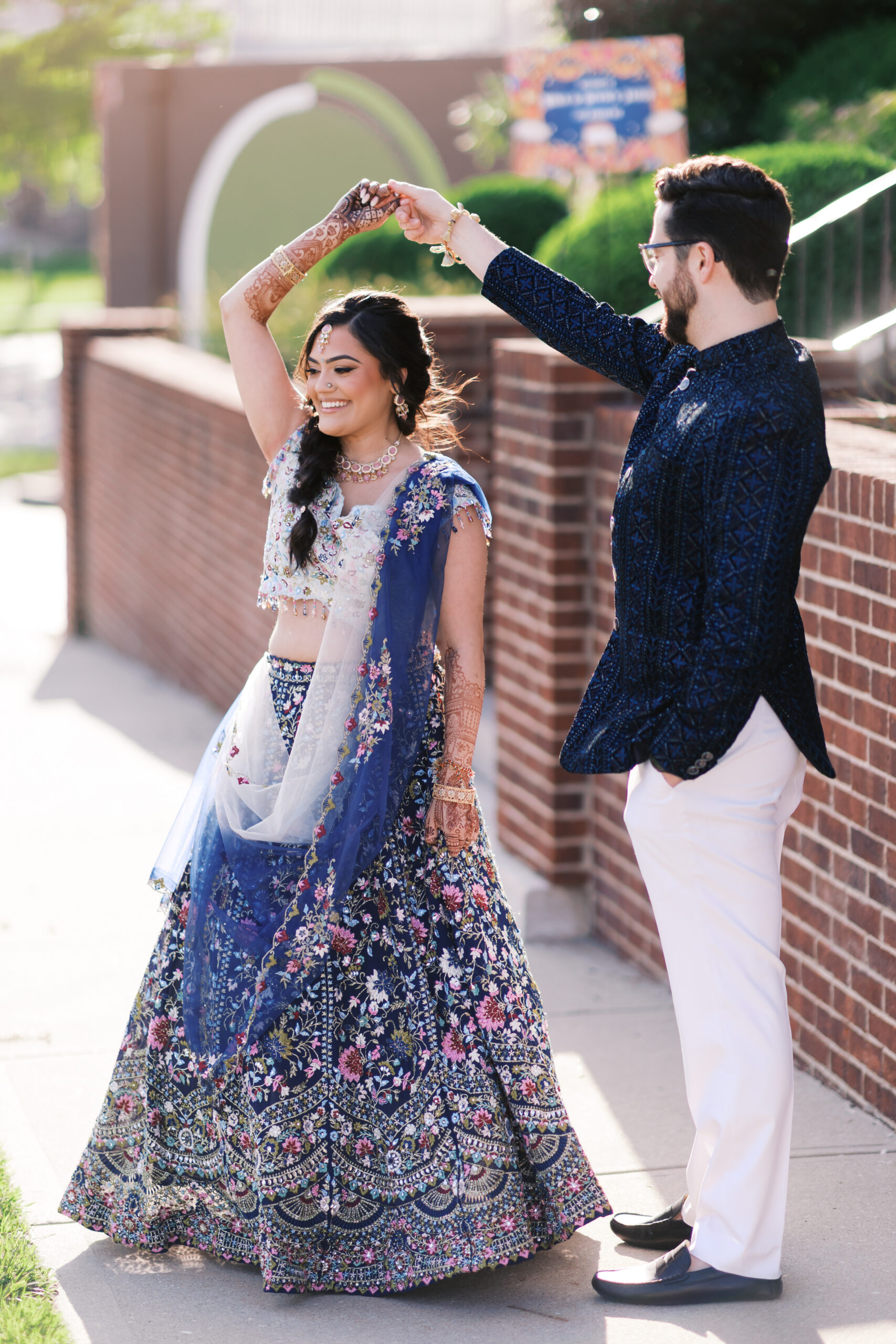 Groom twirling bride in floral lehenga during outdoor wedding festivities.
