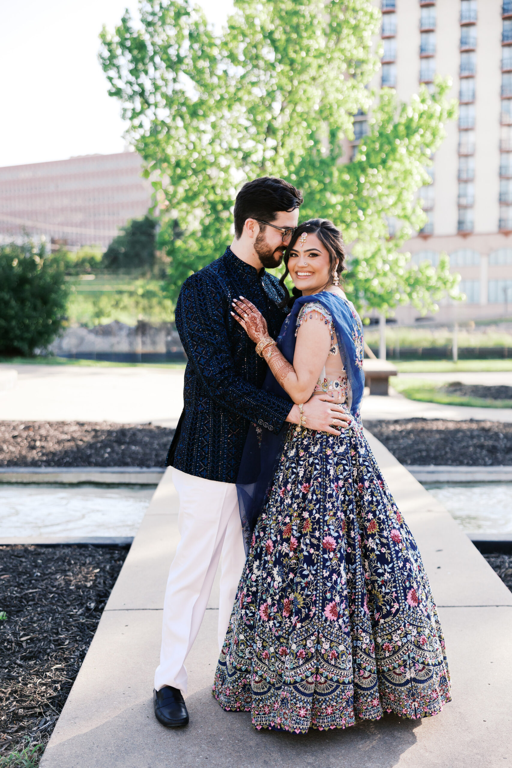 Bride and groom embracing outdoors in traditional Indian wedding attire.