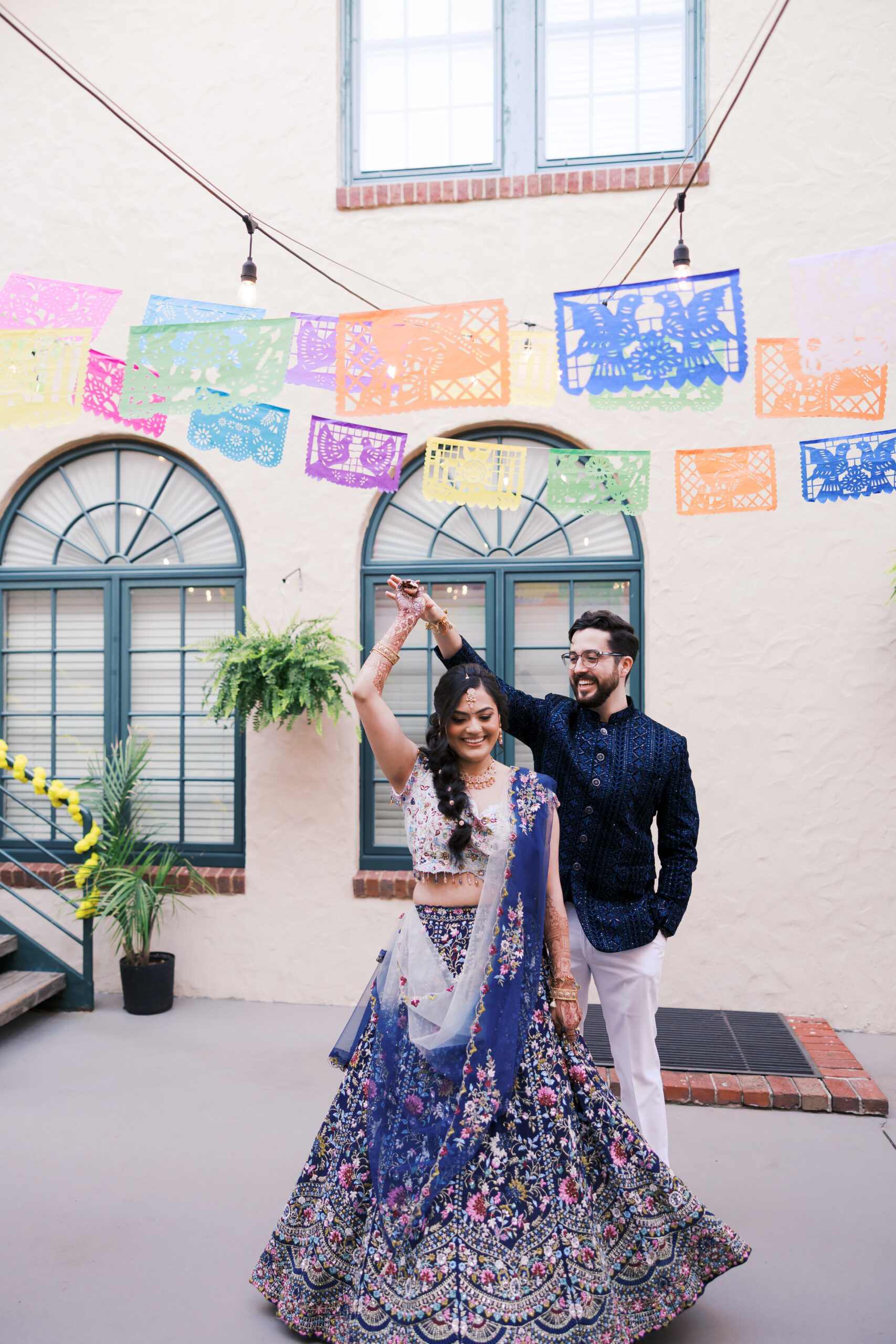Bride twirling under colorful papel picado banners at Jaggo celebration.