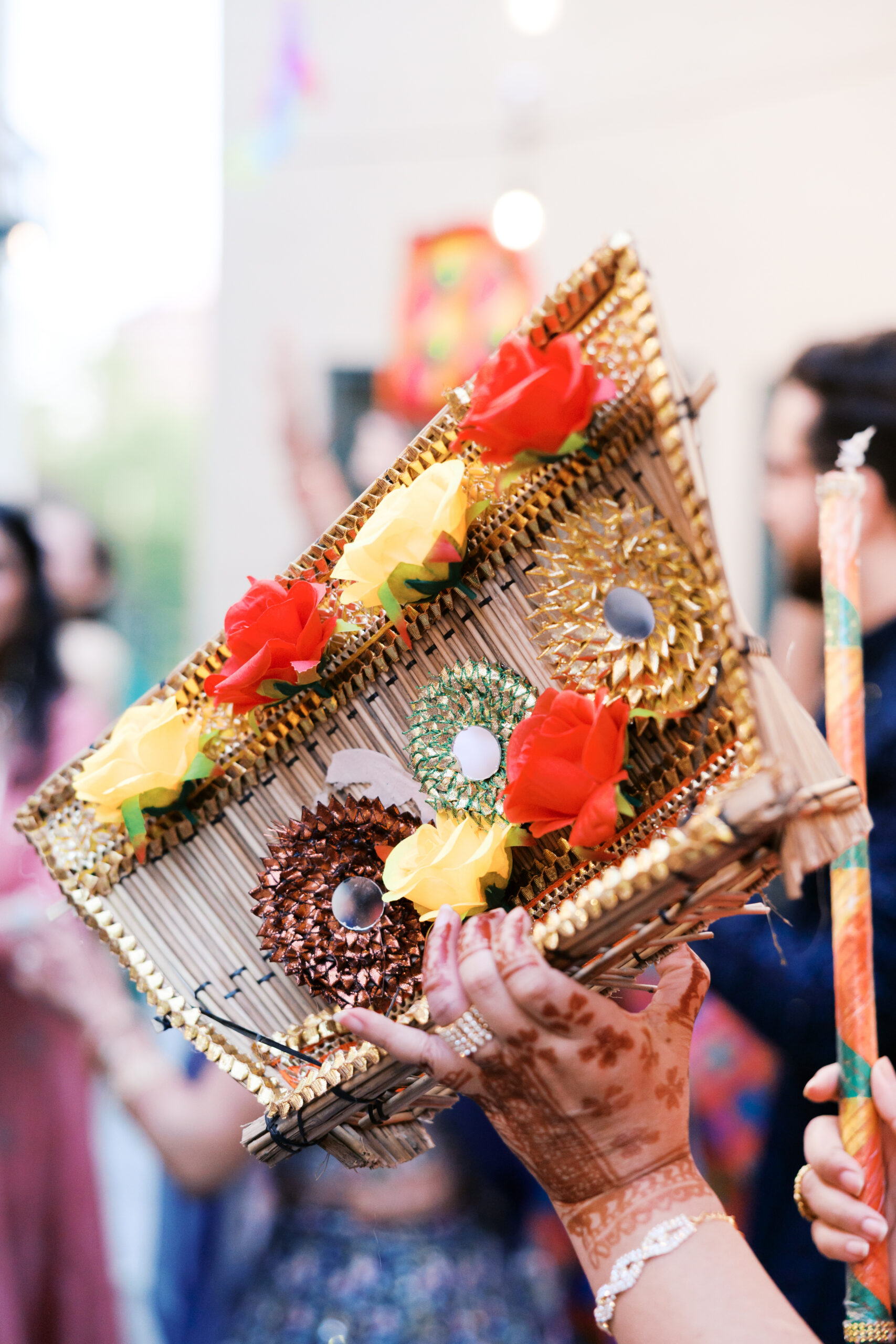 Close-up of decorated Jaggo basket with flowers and gold accents held by mehndi-covered hands.