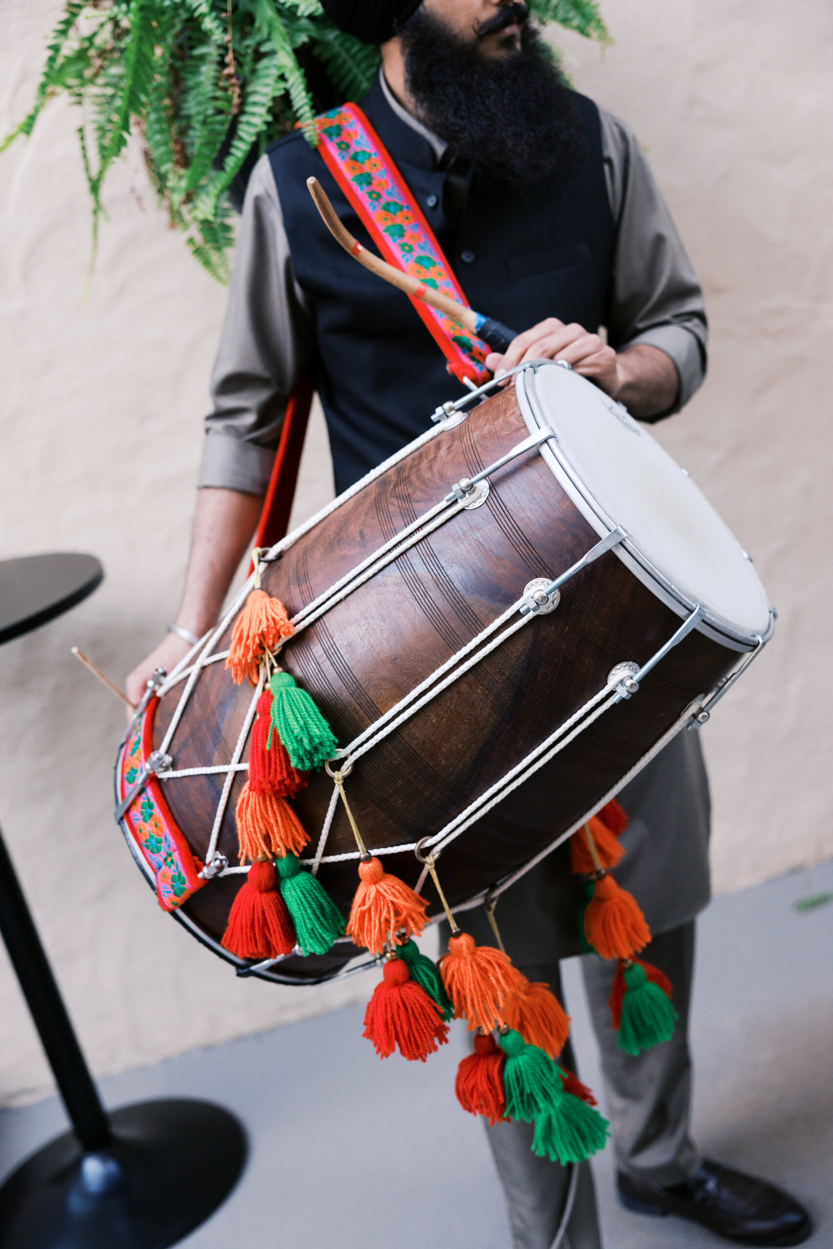 Dhol drummer playing at outdoor South Asian wedding celebration.