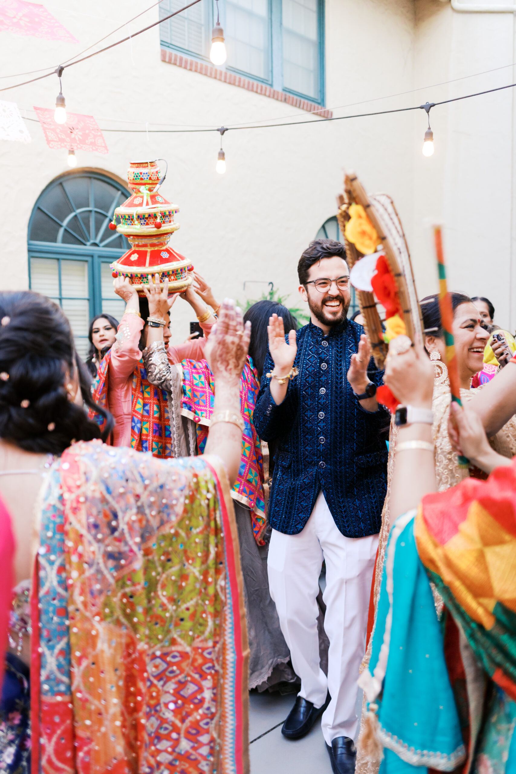 Groom clapping and smiling surrounded by guests at lively Jaggo celebration.