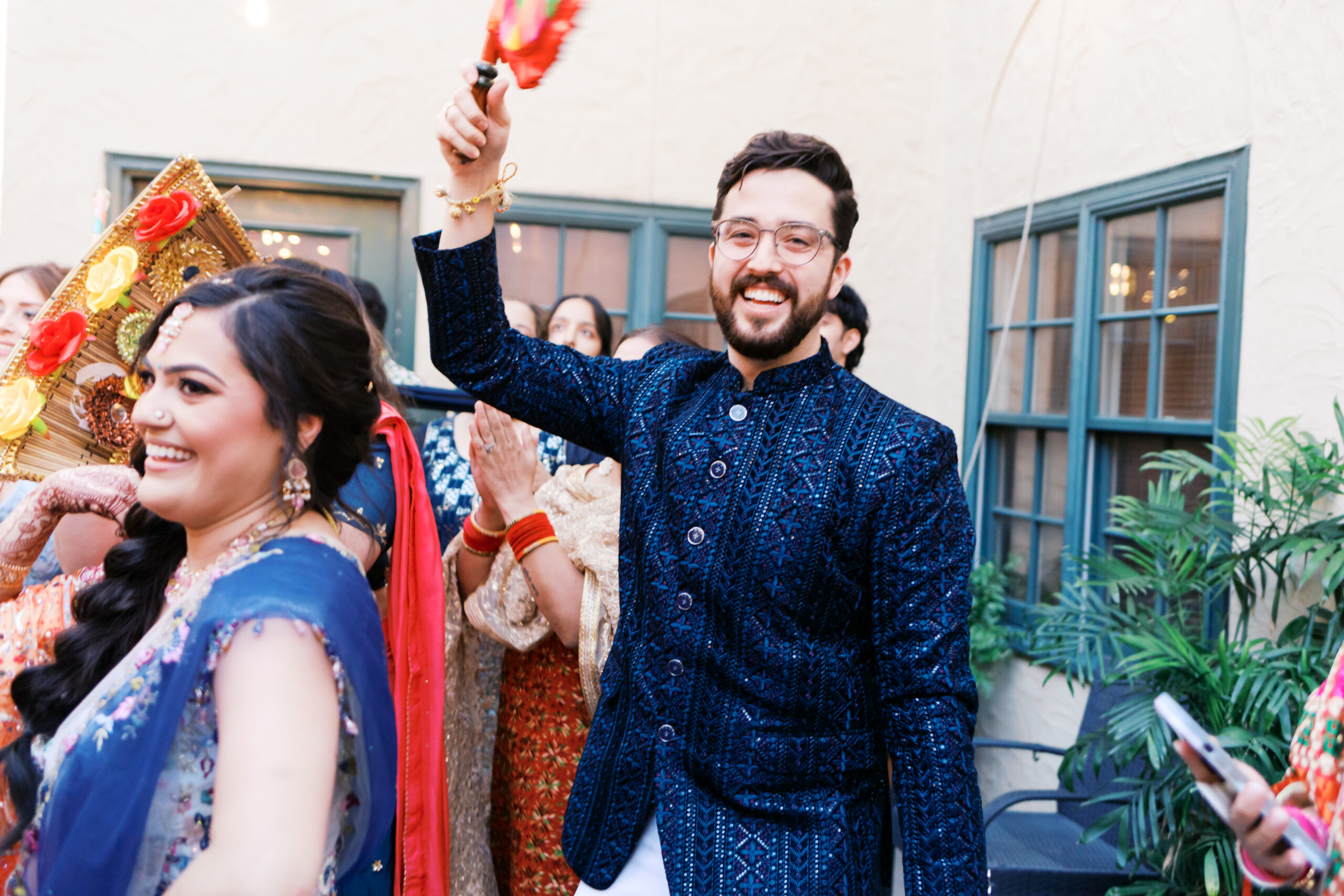 Groom waving colorful Jaggo fan during outdoor Indian wedding festivities.