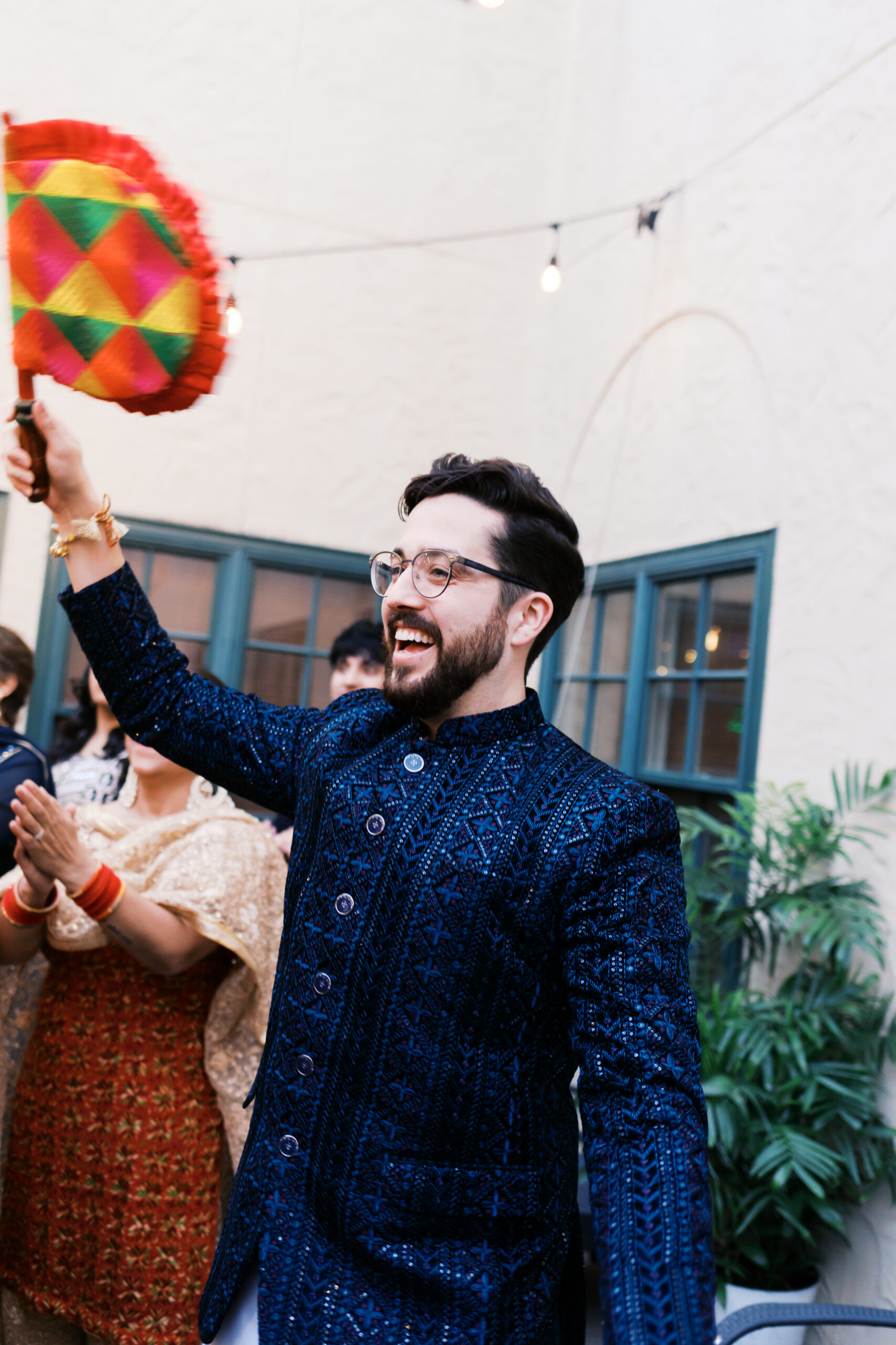 Groom waving colorful Jaggo fan during outdoor Indian wedding.