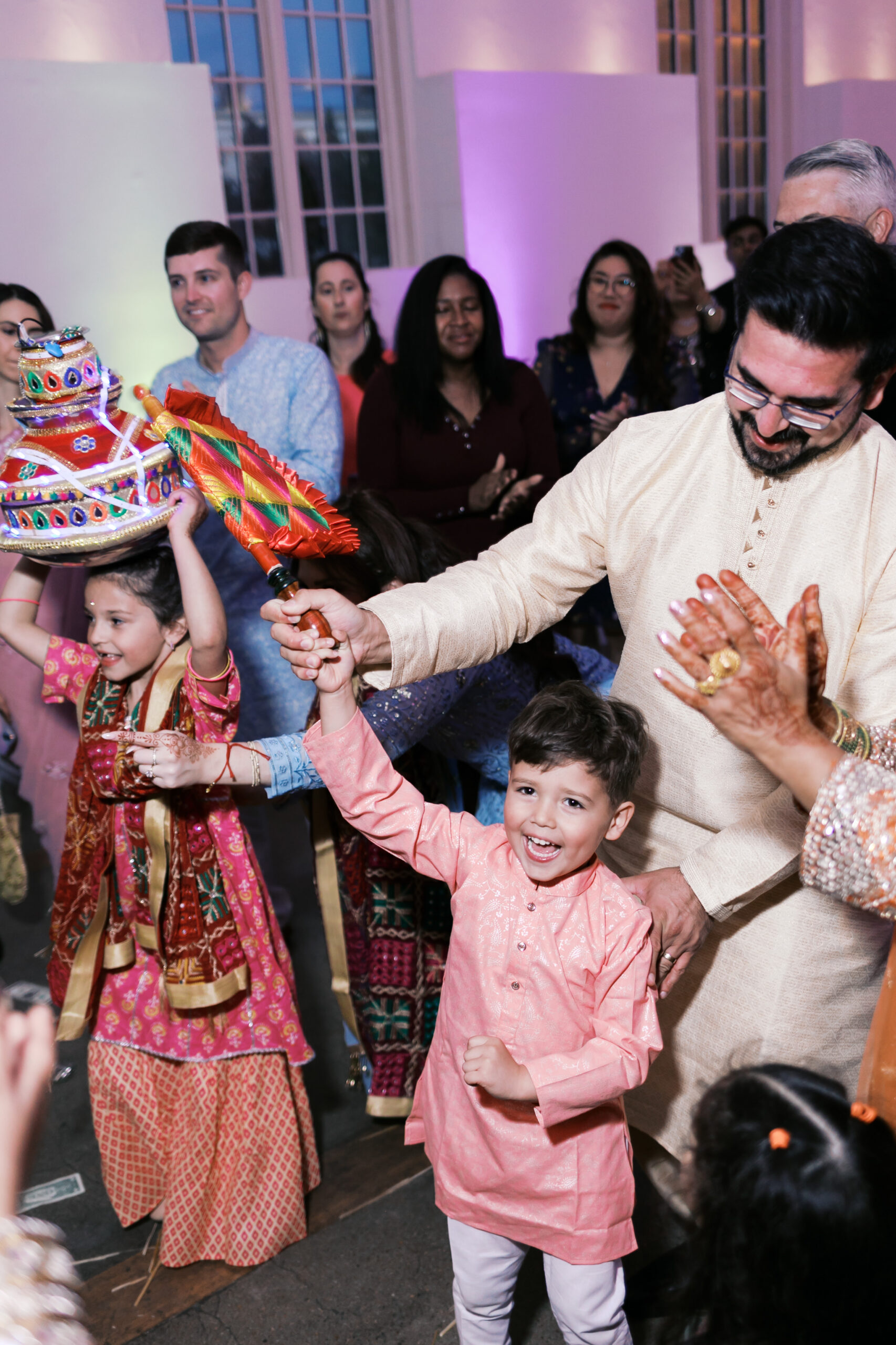 Children dancing with decorated pot and Jaggo stick at wedding reception.
