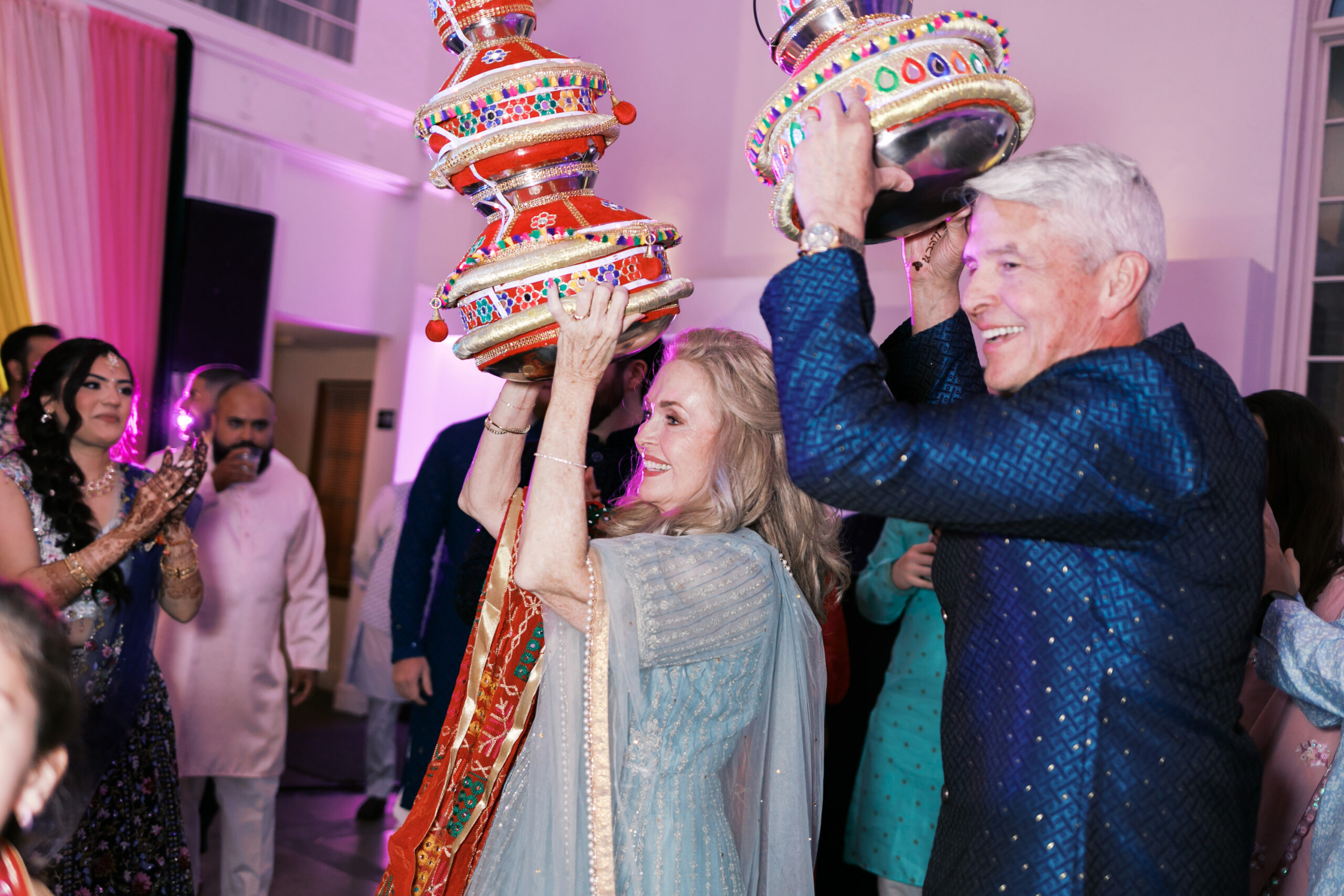 Parents balancing colorful Jaggo pots on their heads during reception celebration.