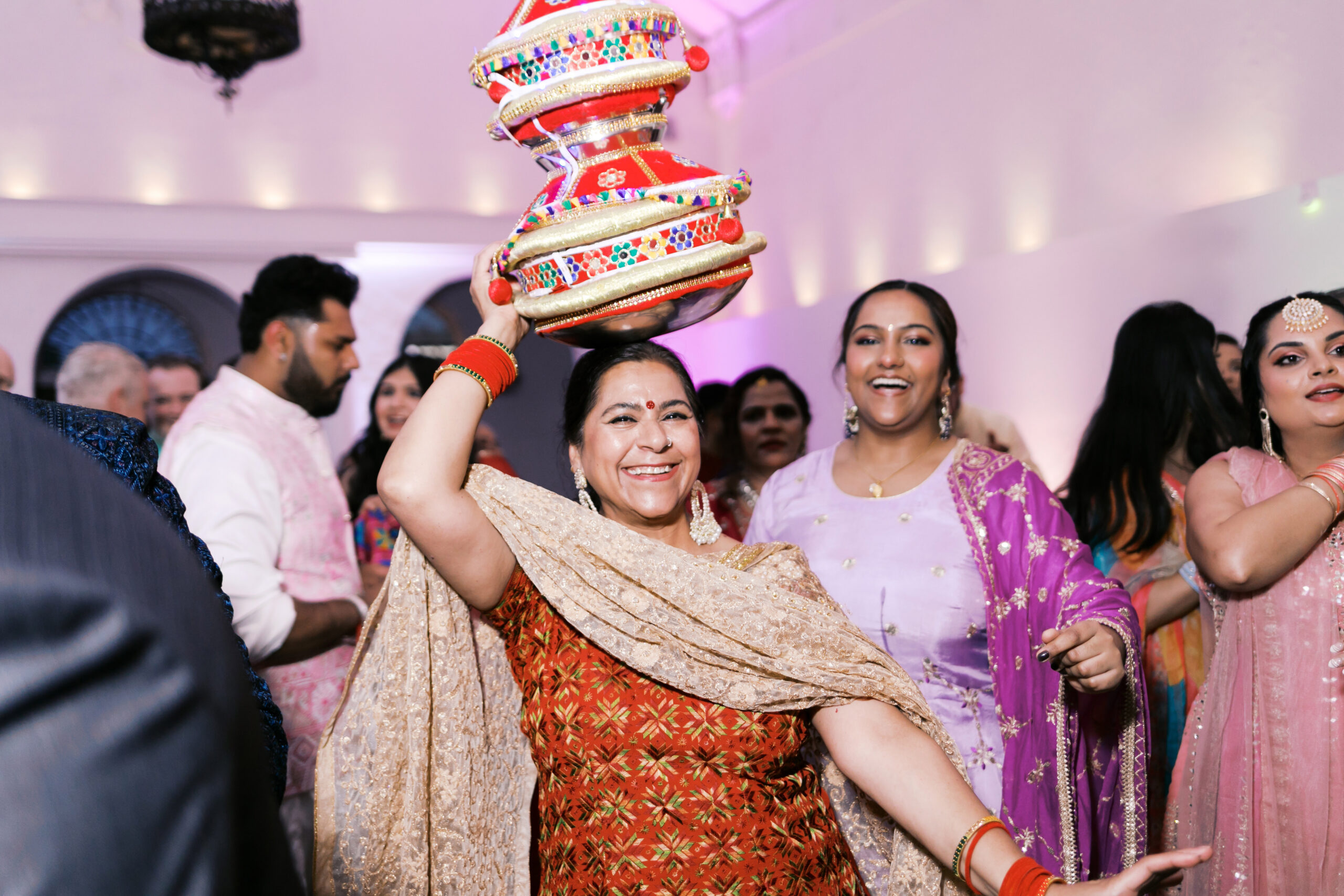 Guest dancing with decorated Jaggo pot on her head under pink and yellow draping.