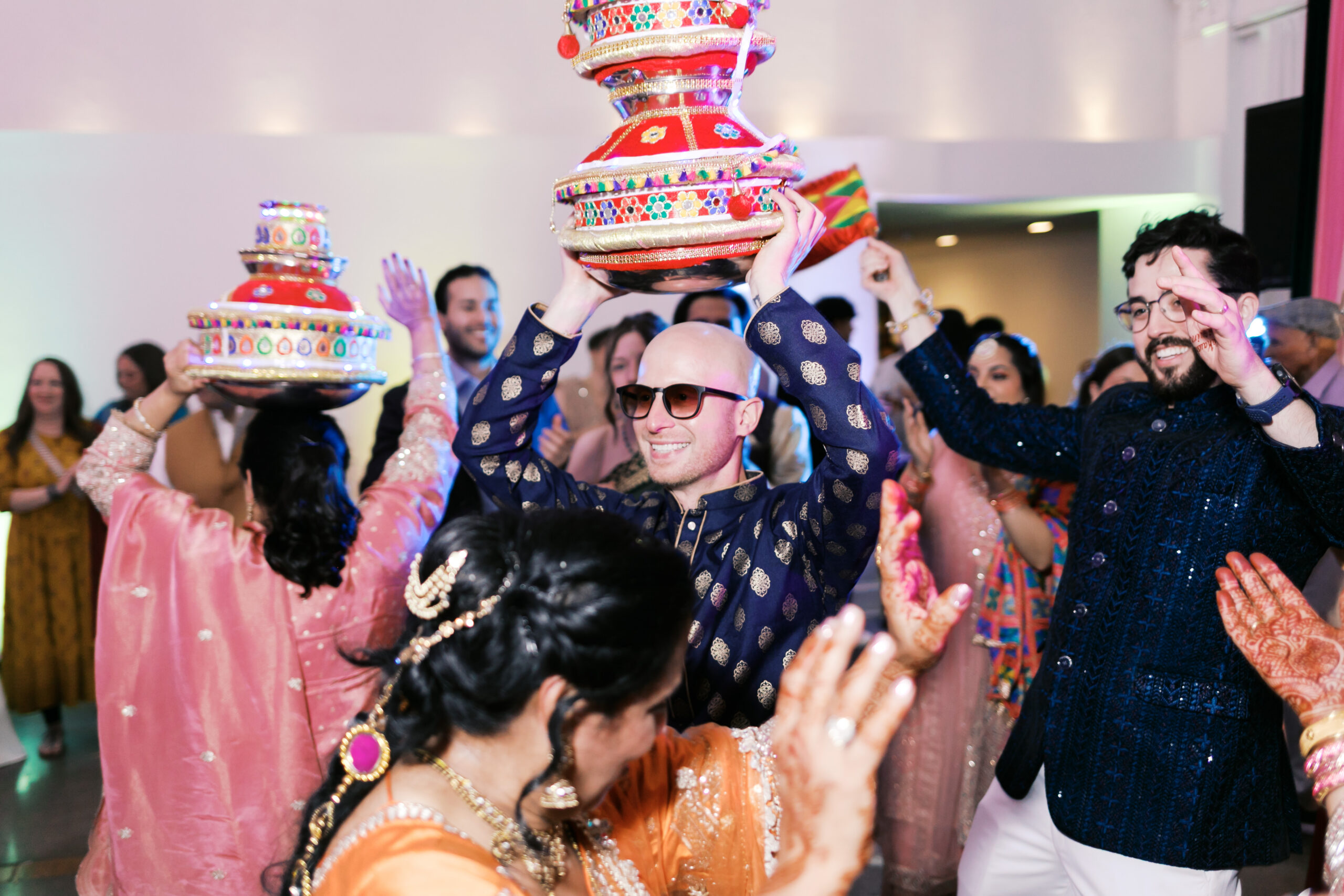 Guests raising decorated pots while dancing at vibrant Indian wedding reception.