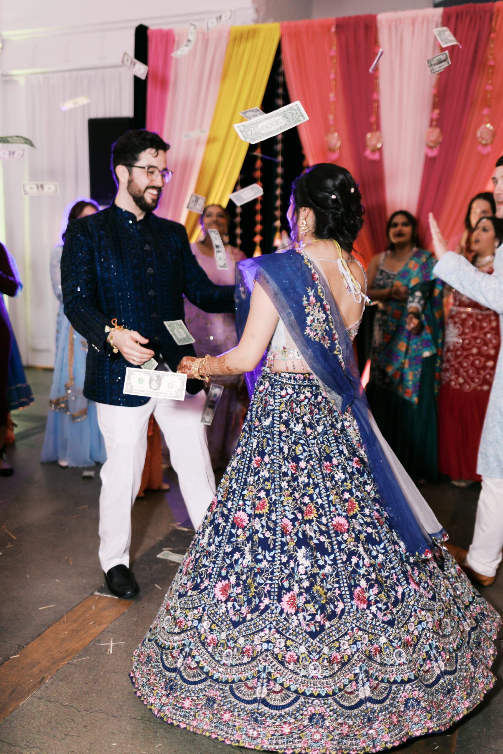 Bride and groom dancing as dollar bills are tossed during Jaggo celebration.