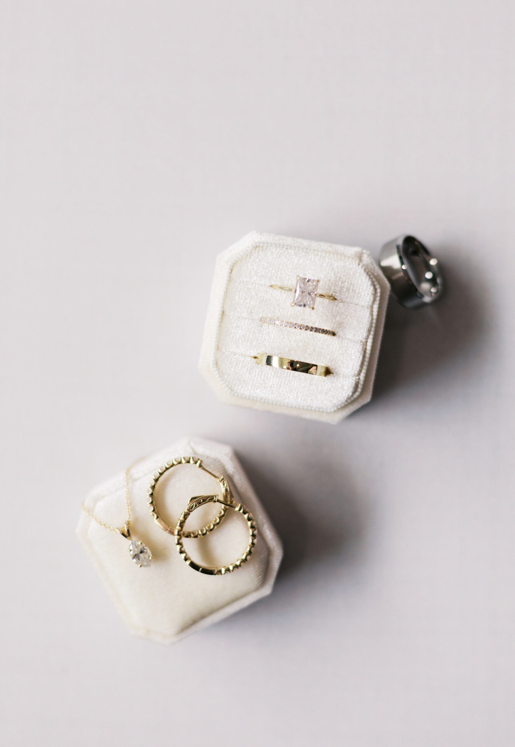 Close-up of wedding rings and diamond jewelry arranged in velvet ring boxes on a soft white surface.