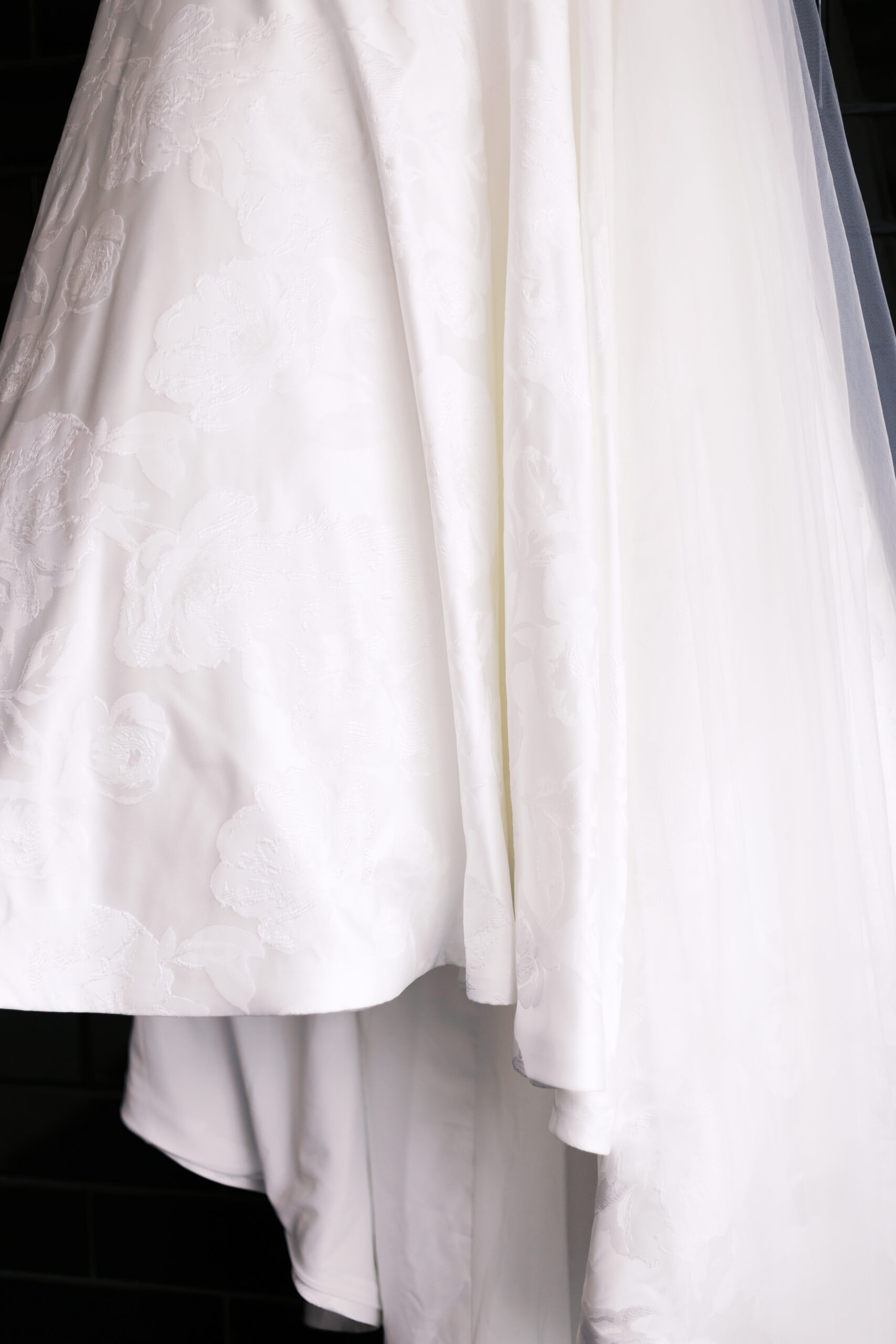 Close-up detail of layered wedding dress fabric with floral texture and soft folds in natural light.