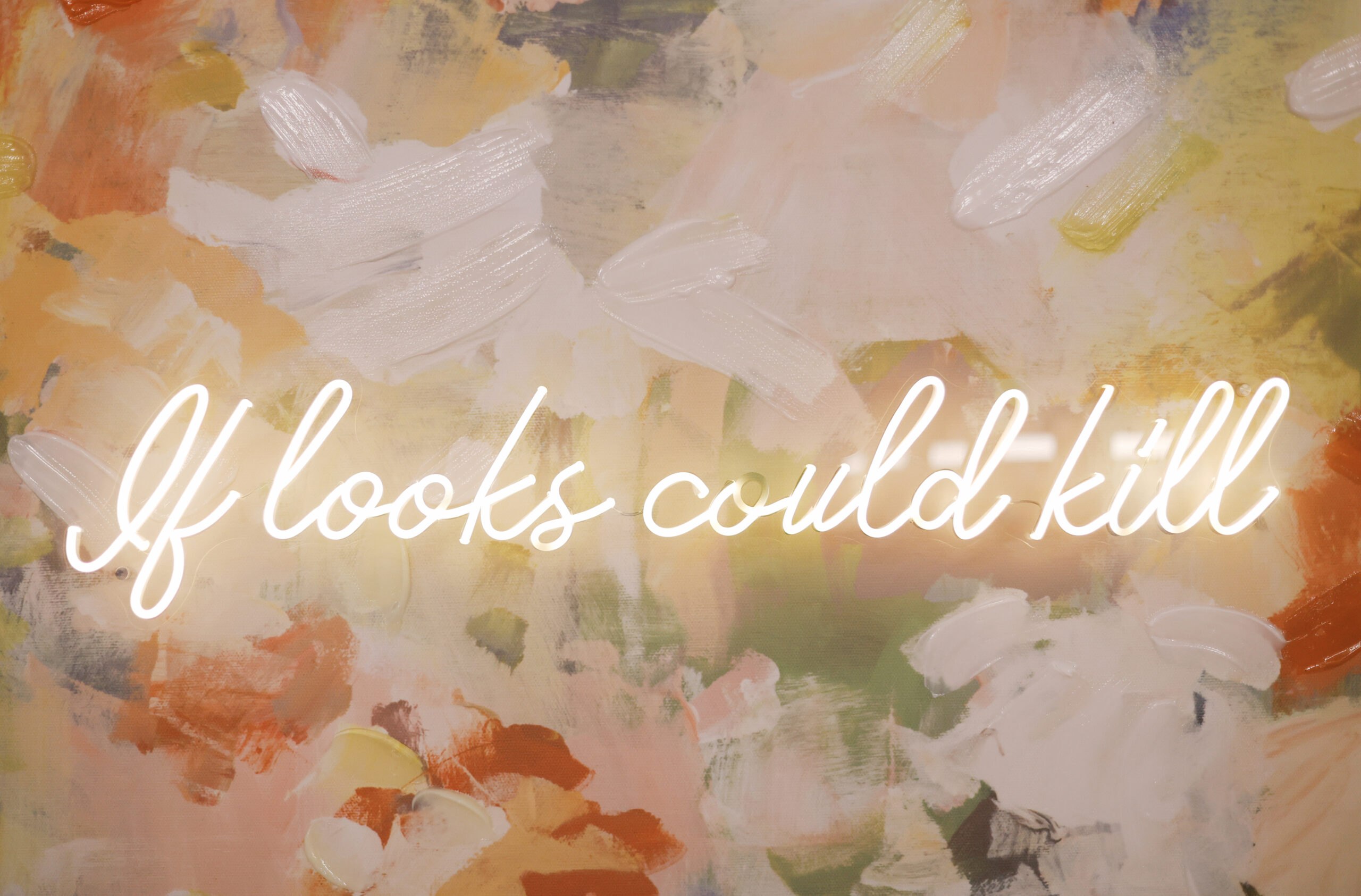 Neon sign reading “If looks could kill” mounted on a colorful abstract wall inside the wedding venue.