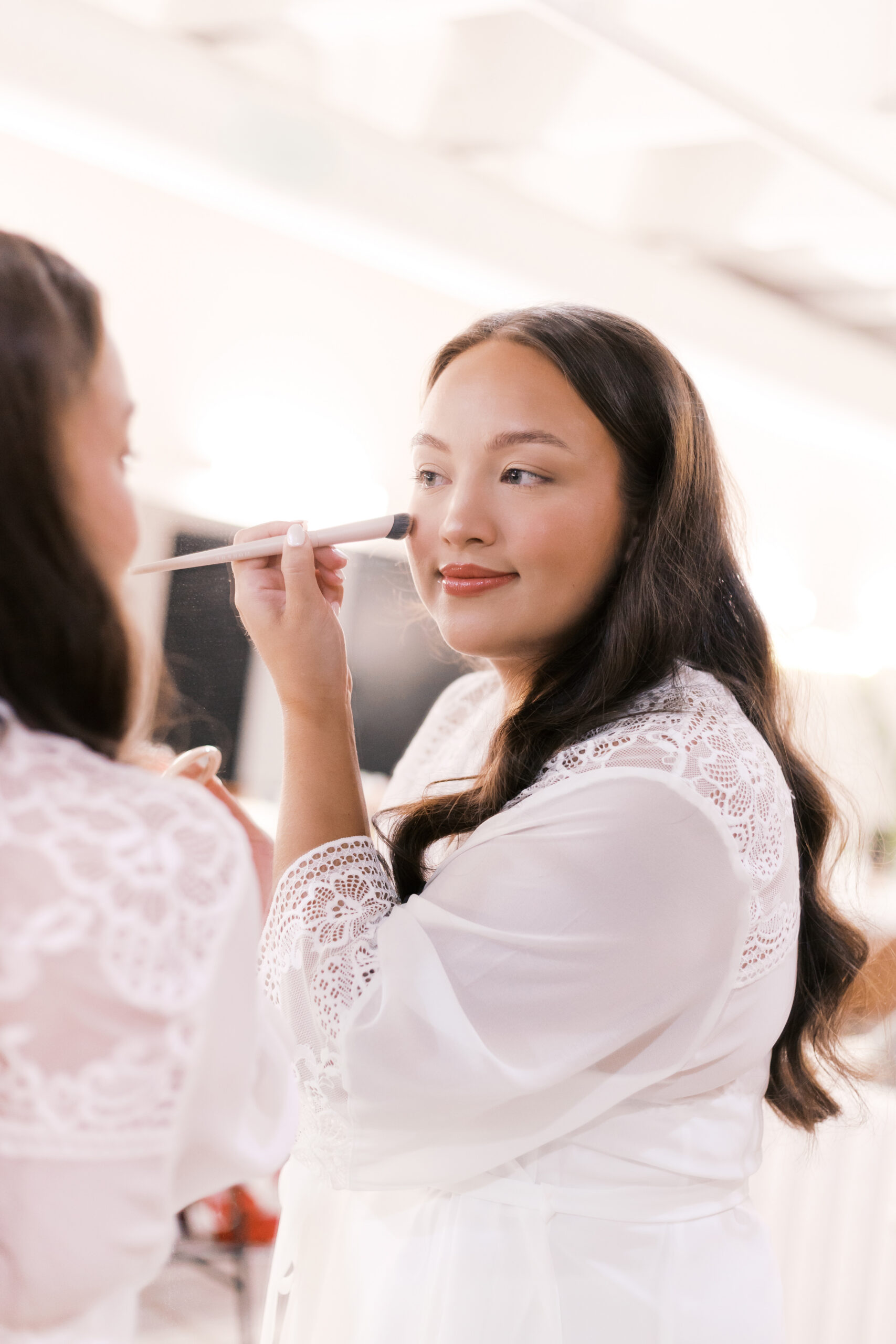 Bride in a white lace robe having makeup applied during wedding morning preparations at The Maverick in Kansas City.