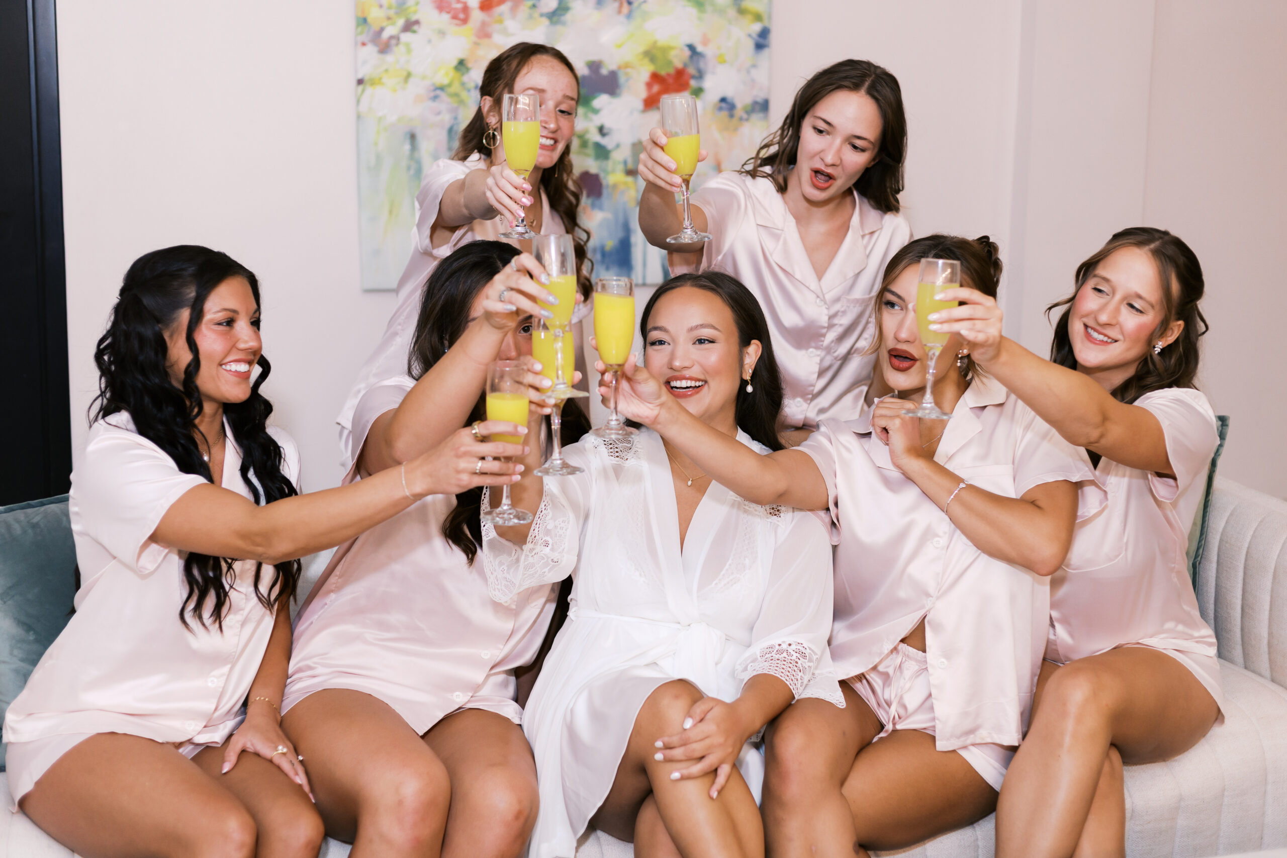 Bride and bridesmaids in matching pajamas raise champagne flutes together during wedding morning at The Maverick.