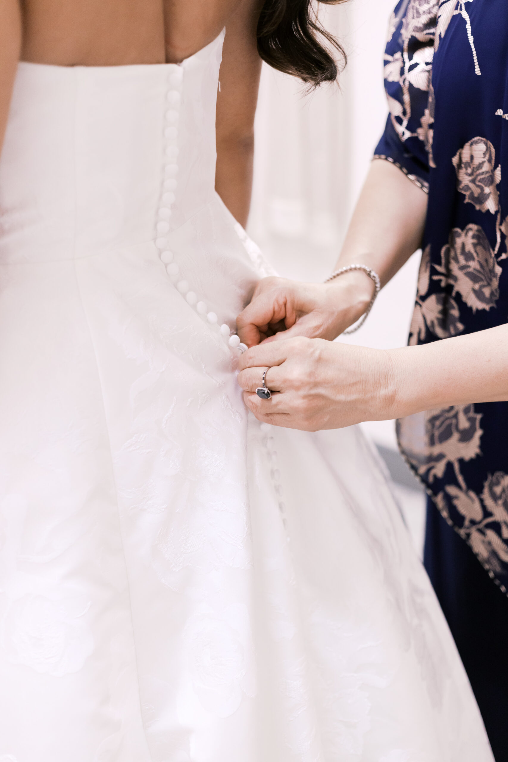 Side view of a wedding dress being buttoned up the back, highlighting fabric texture and fitted bodice.