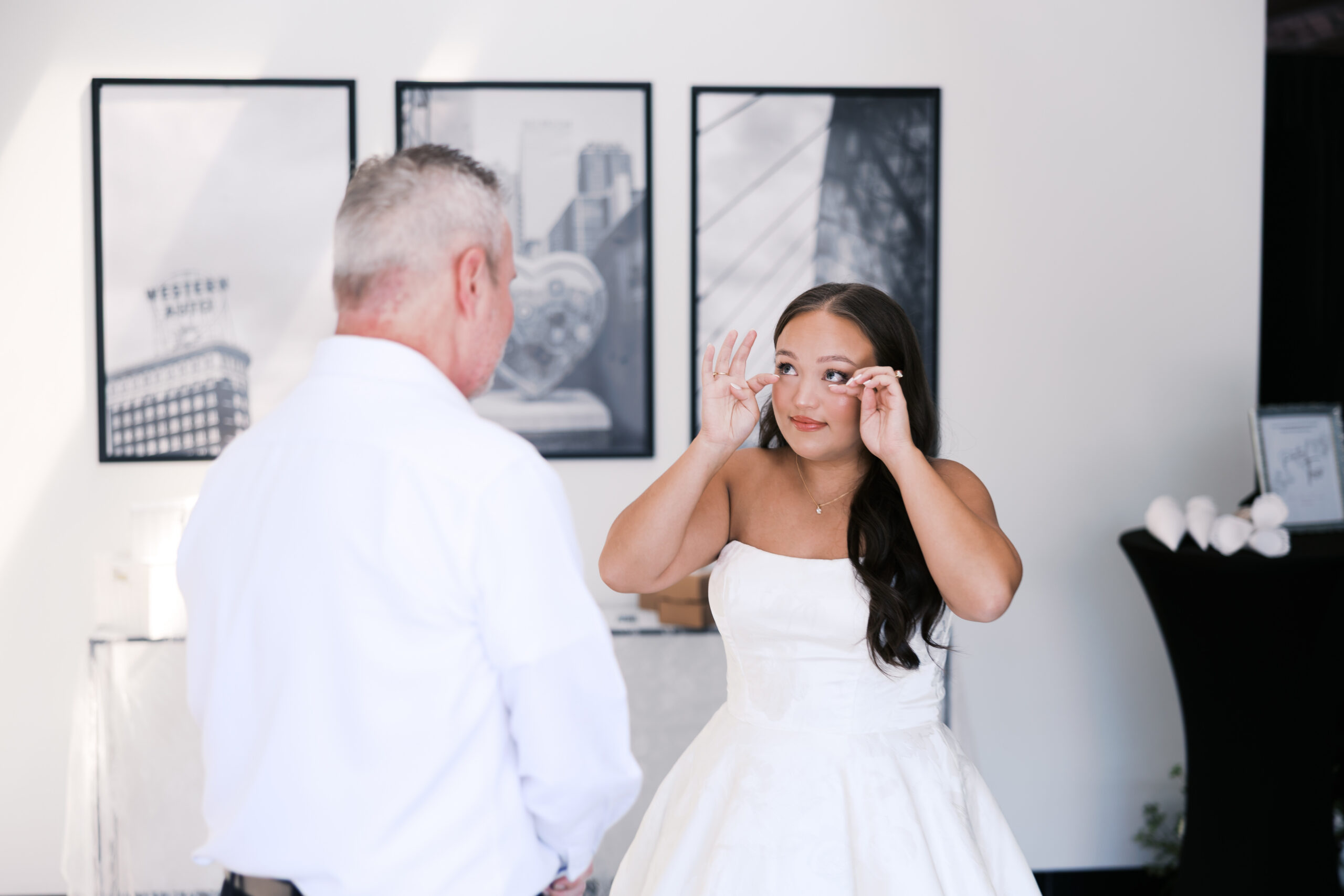 Bride wipes beneath her eyes while standing across from her father during an emotional first-look moment.