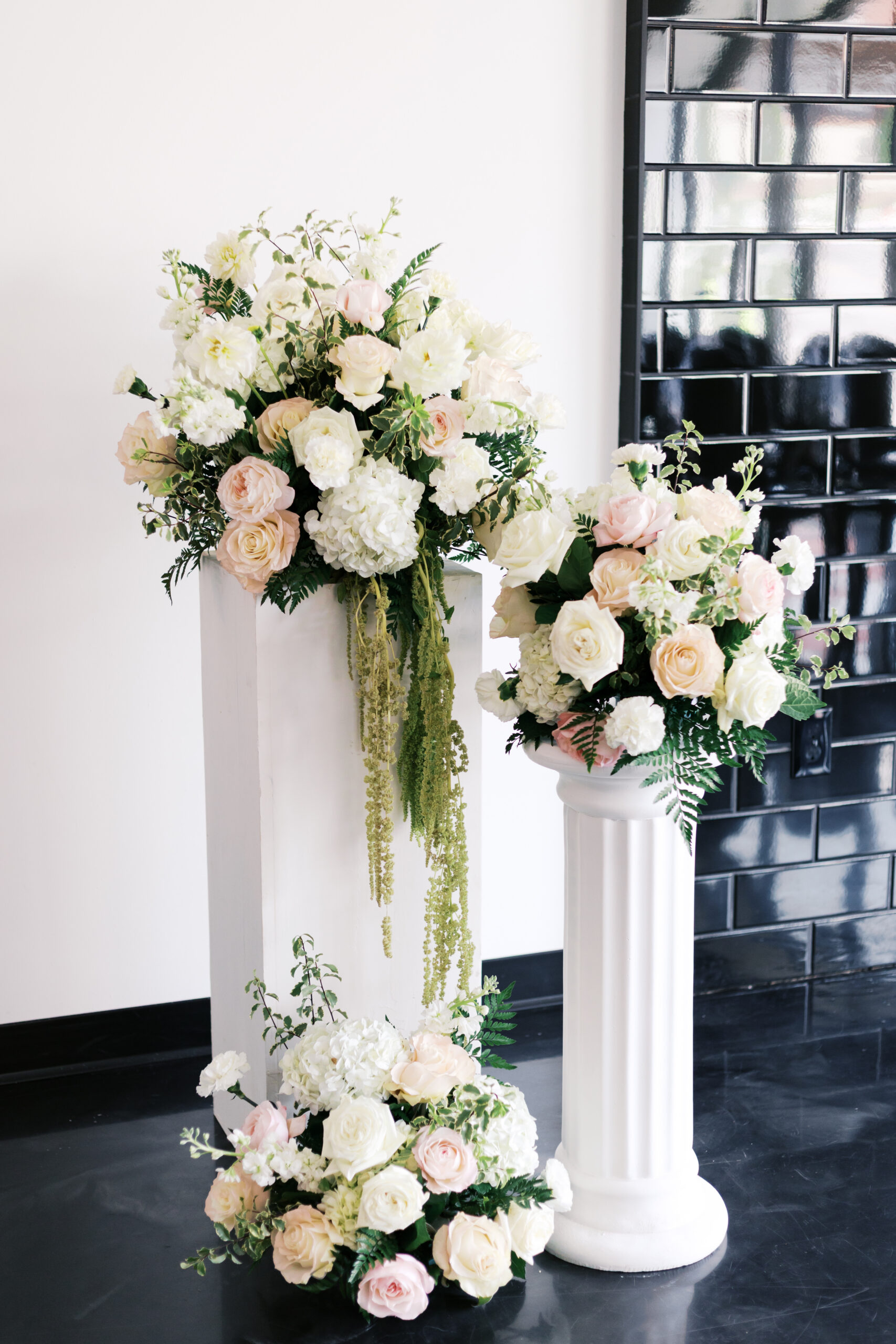 White and blush floral arrangements displayed on pedestal columns at a modern indoor wedding ceremony.