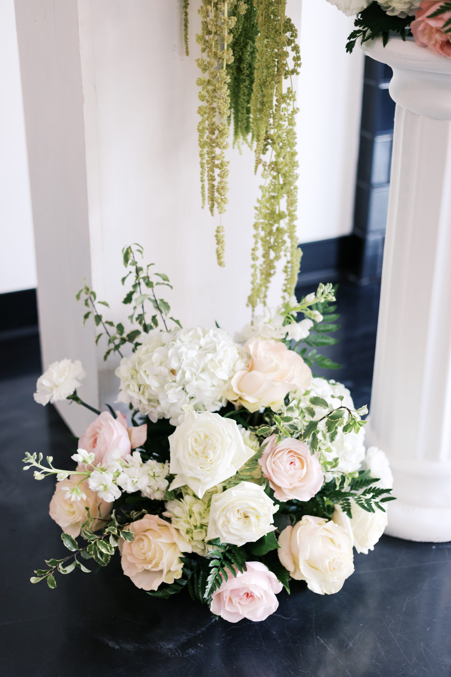 White and blush floral arrangements displayed on pedestal columns at a modern indoor wedding ceremony.