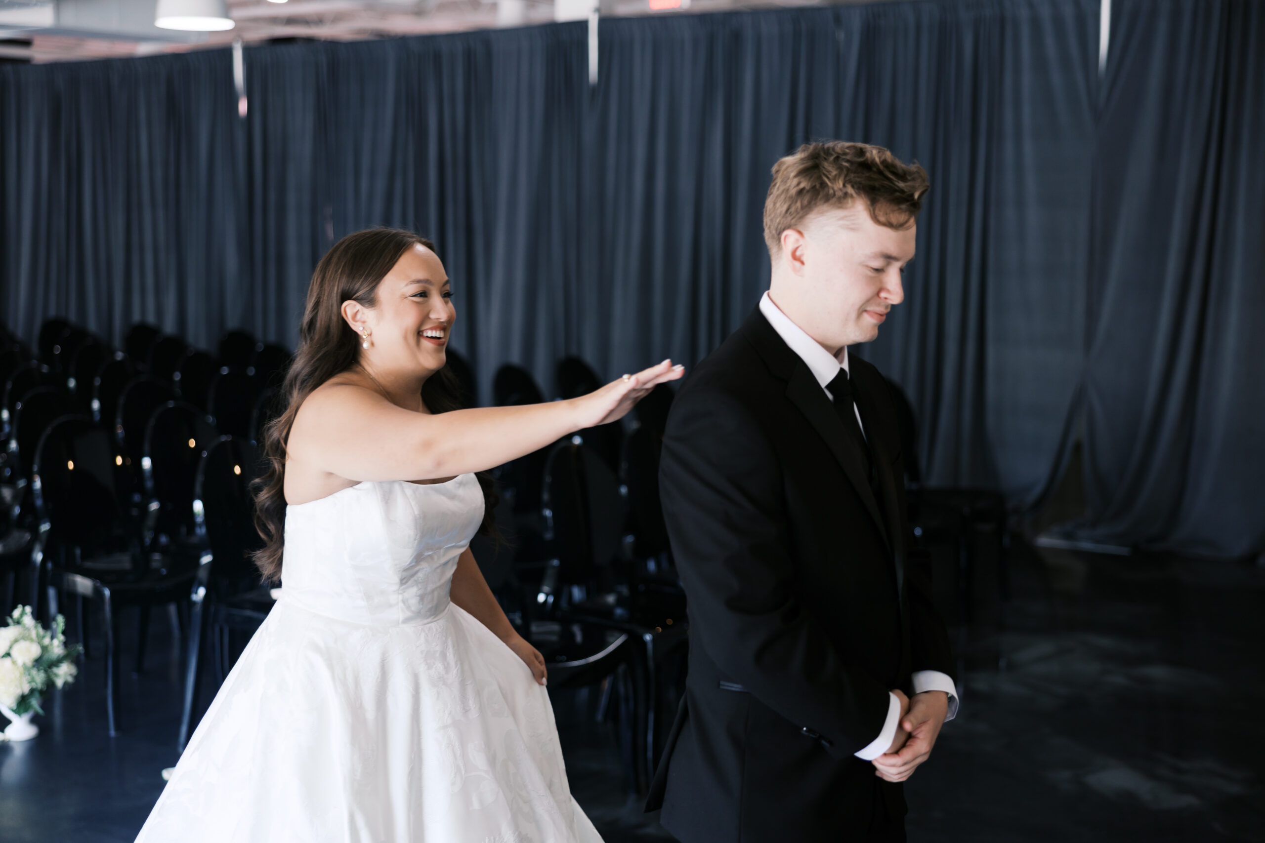 Bride reaches out toward the groom’s shoulder from behind during a first-look moment inside the ceremony space.
