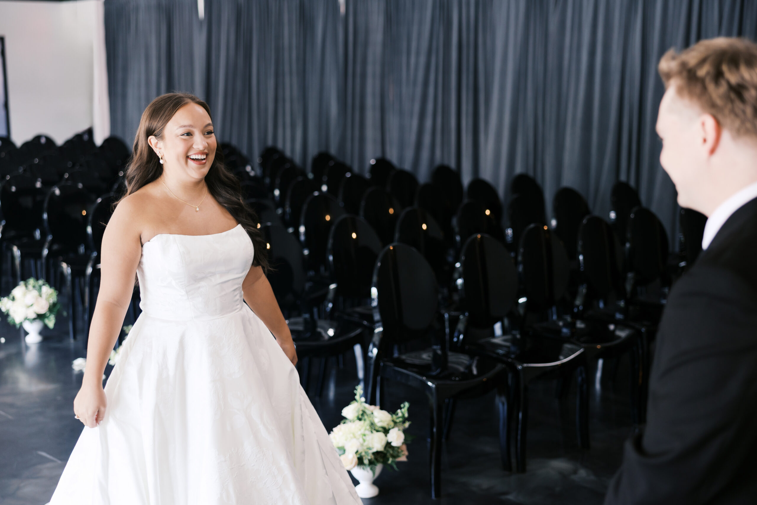 Bride smiles while standing in the ceremony aisle facing the groom before their first look.