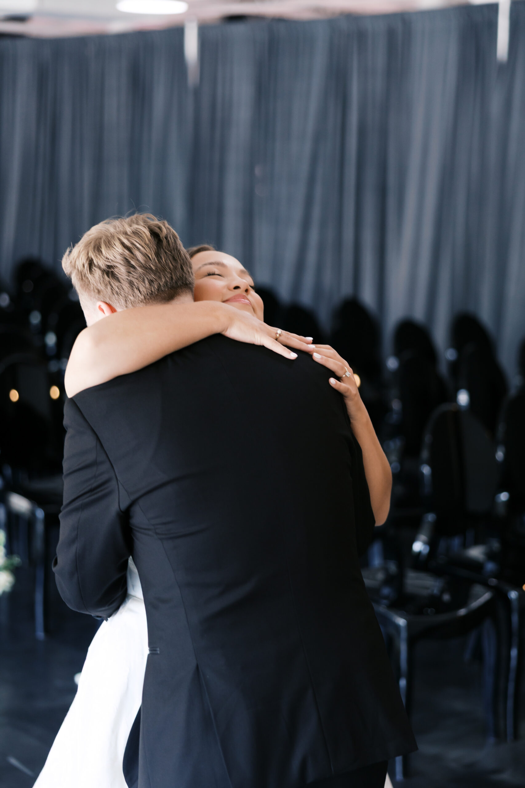 Bride and groom embrace in the ceremony space, surrounded by rows of black chairs.