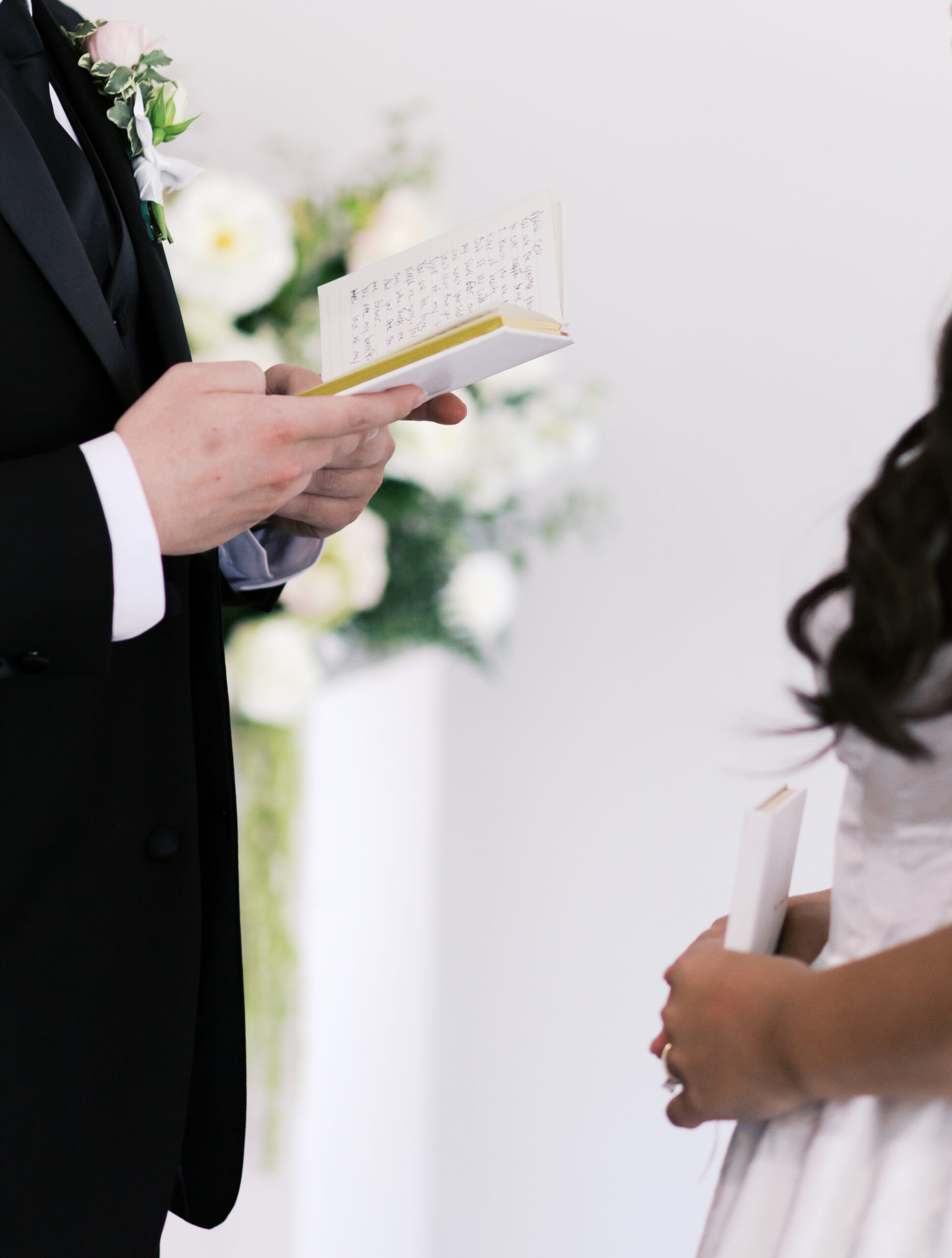 Close-up of groom’s hands holding an open vow book with handwritten notes during the ceremony.