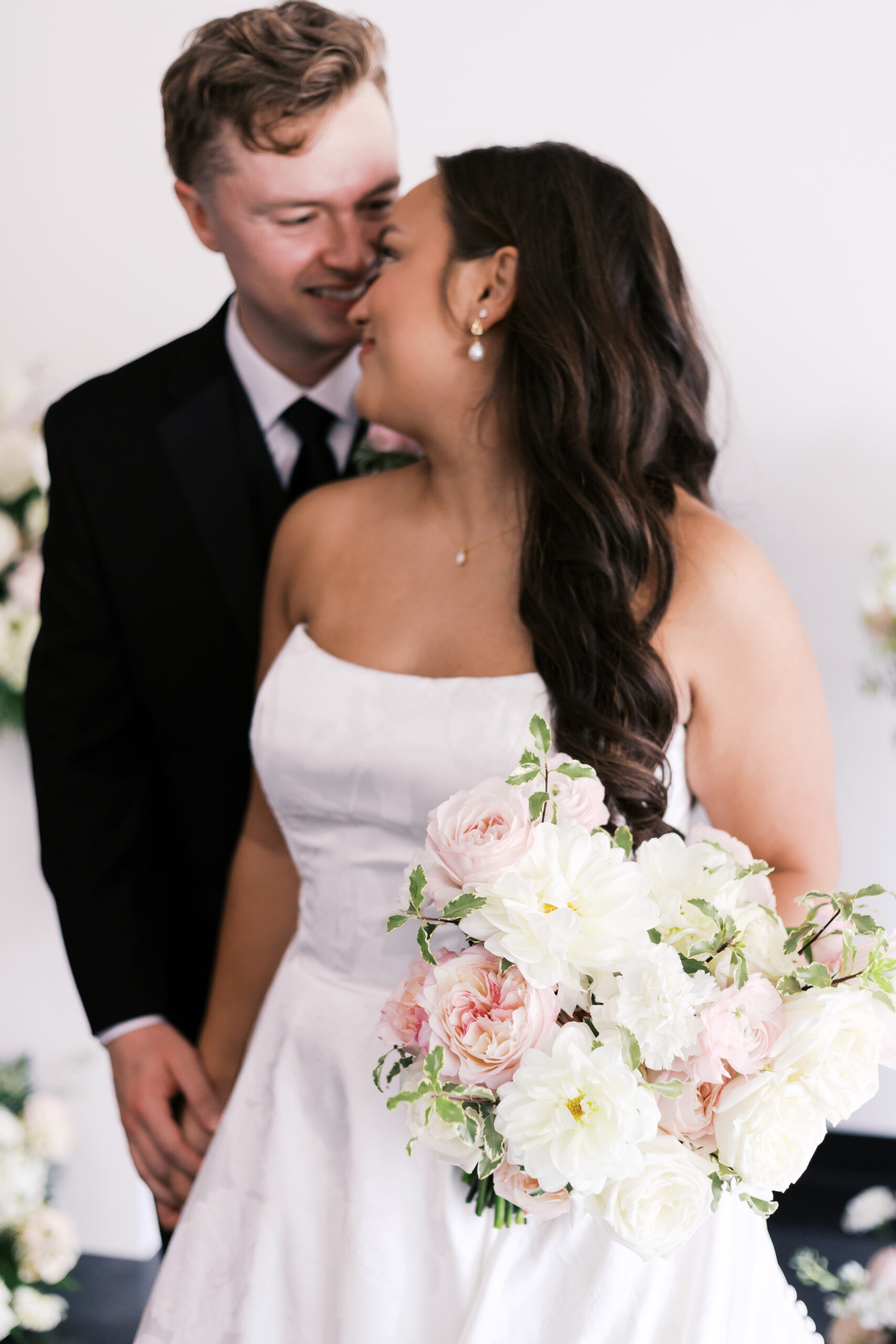 Bride looking back at groom as he smiles at her and holds her hand. She's holding a pink and white bouquet in her hand.