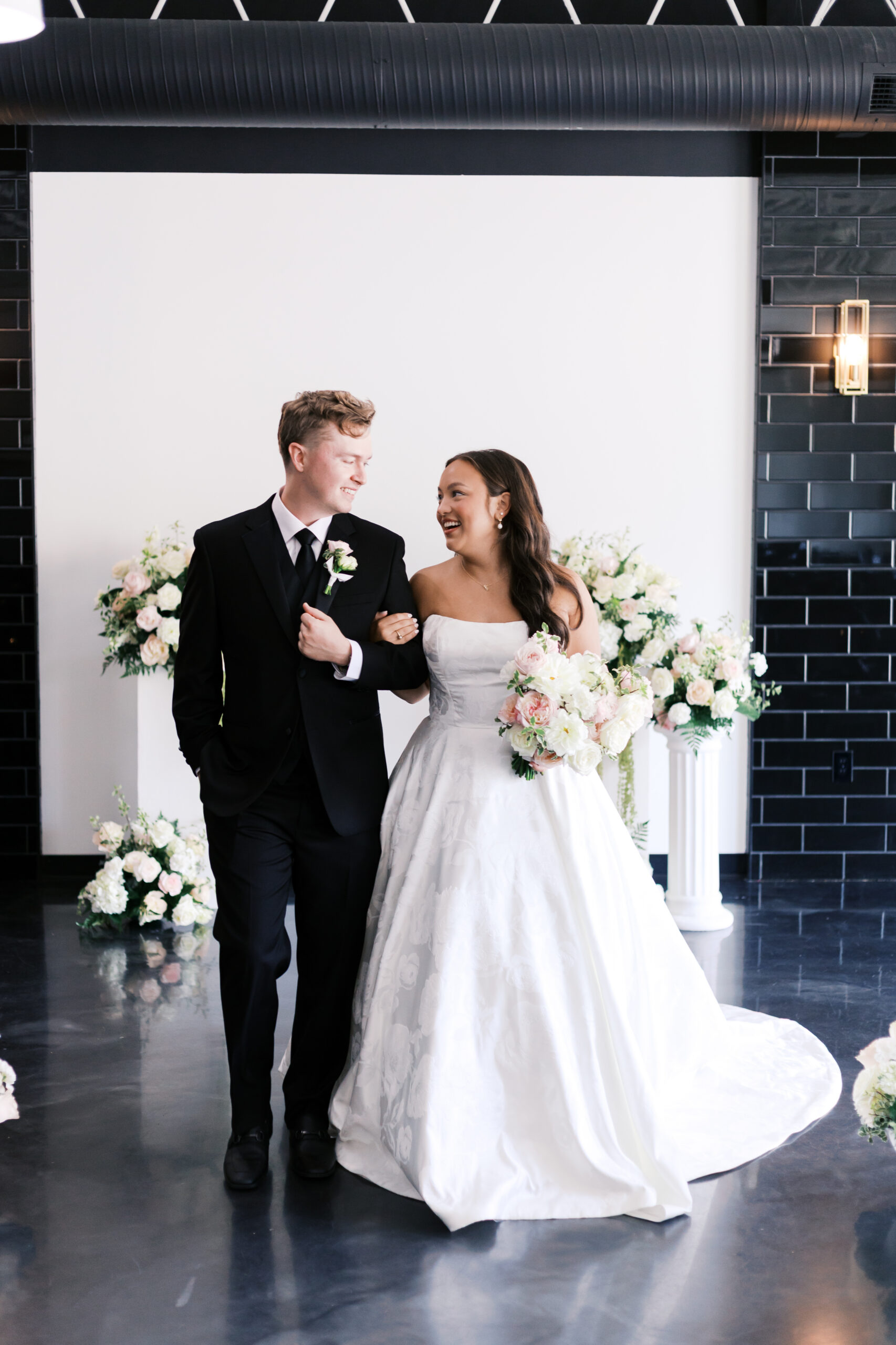 Bride and groom walking arm and arm down an aisle looking at each other and smiling.