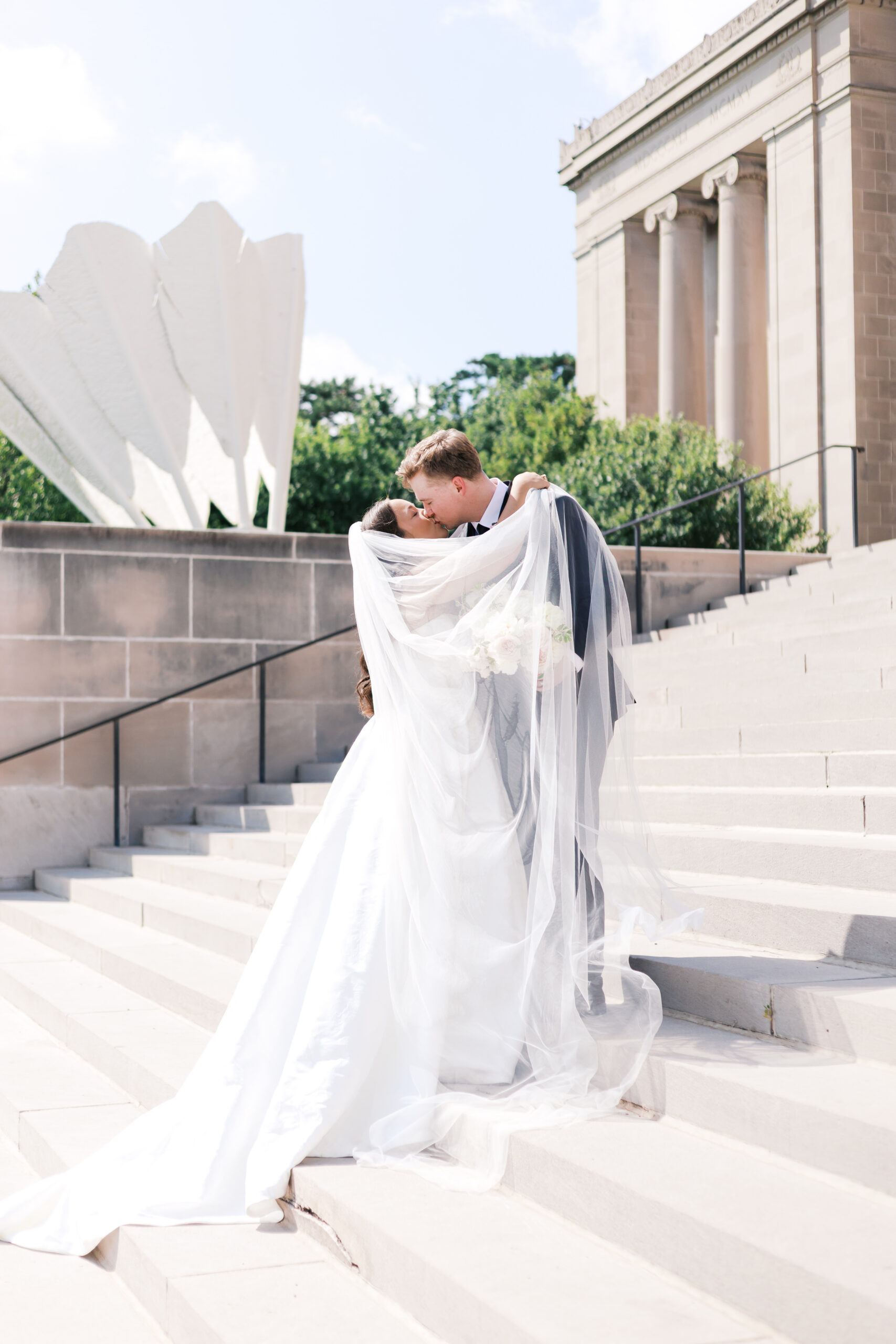Bride and groom kissing on steps with bride's veil flowing in the wind.