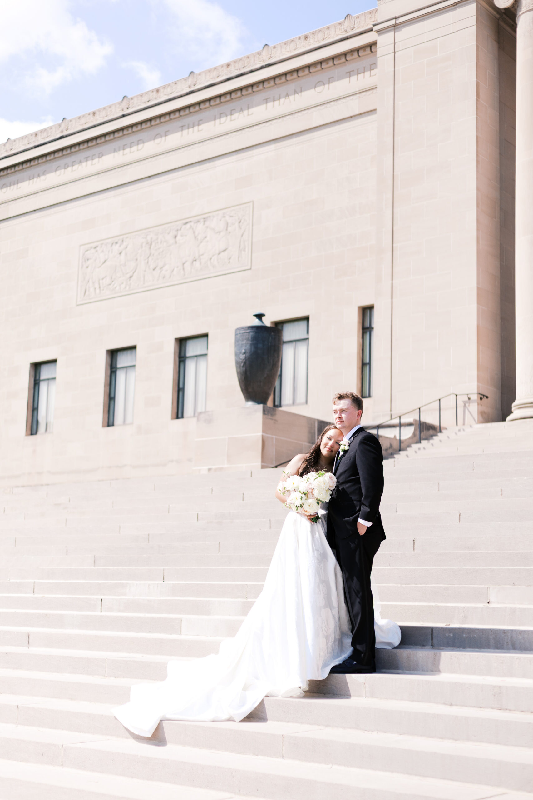 Bride leaning against groom on steps in front of a building.