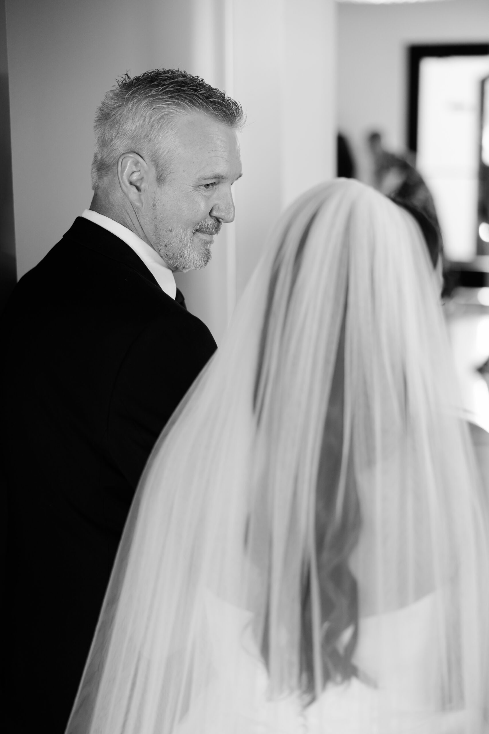 Black and white photo of man in suit standing with bride in veil.