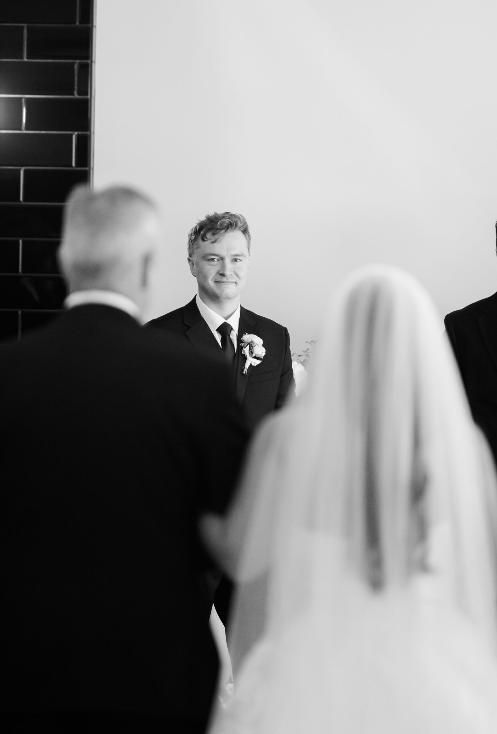 Black and white photo of groom smiling at bride during ceremony.
