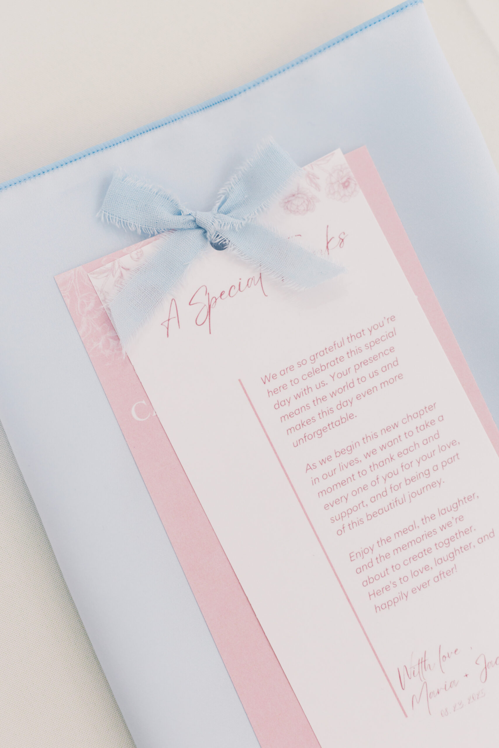 Wedding menu card with pink and blue design tied with light blue ribbon.