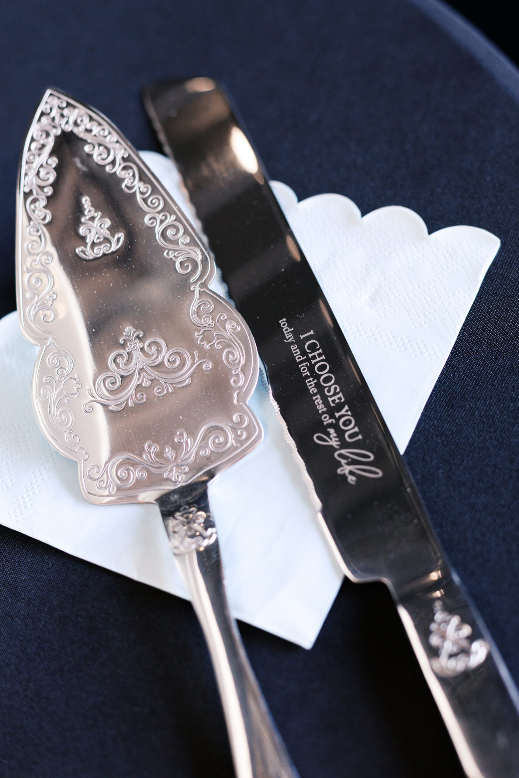 Decorative silver cake server and knife with engraved text on white napkin.