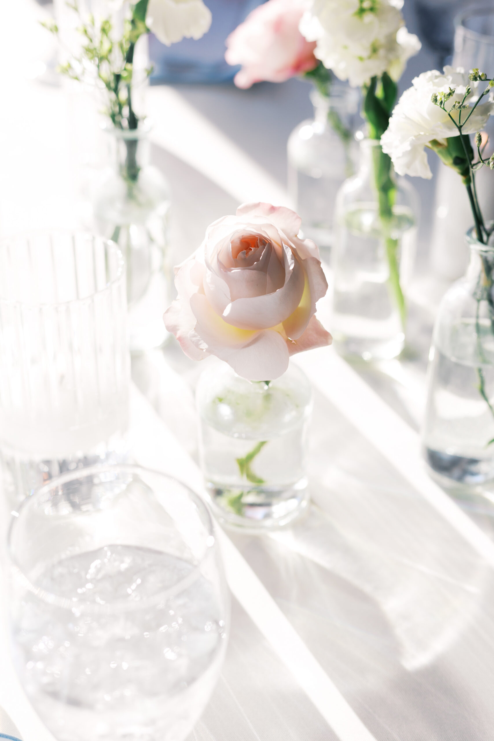 Close-up of blush pink rose in small glass vase on white table.