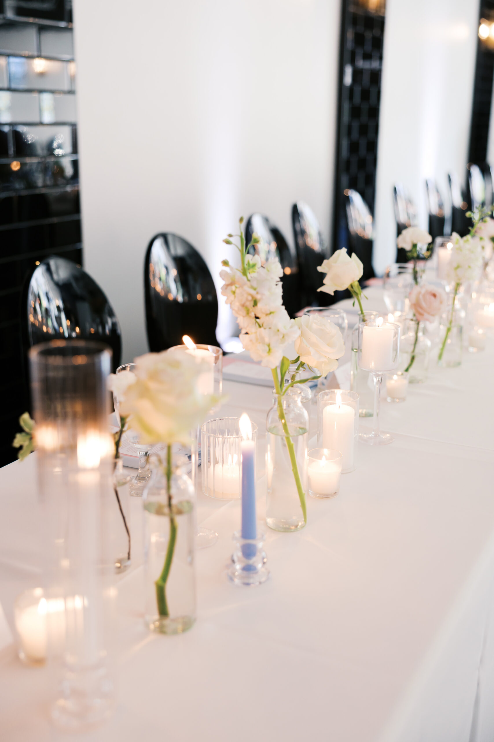 Long head table with white flowers, candles, and black chairs.