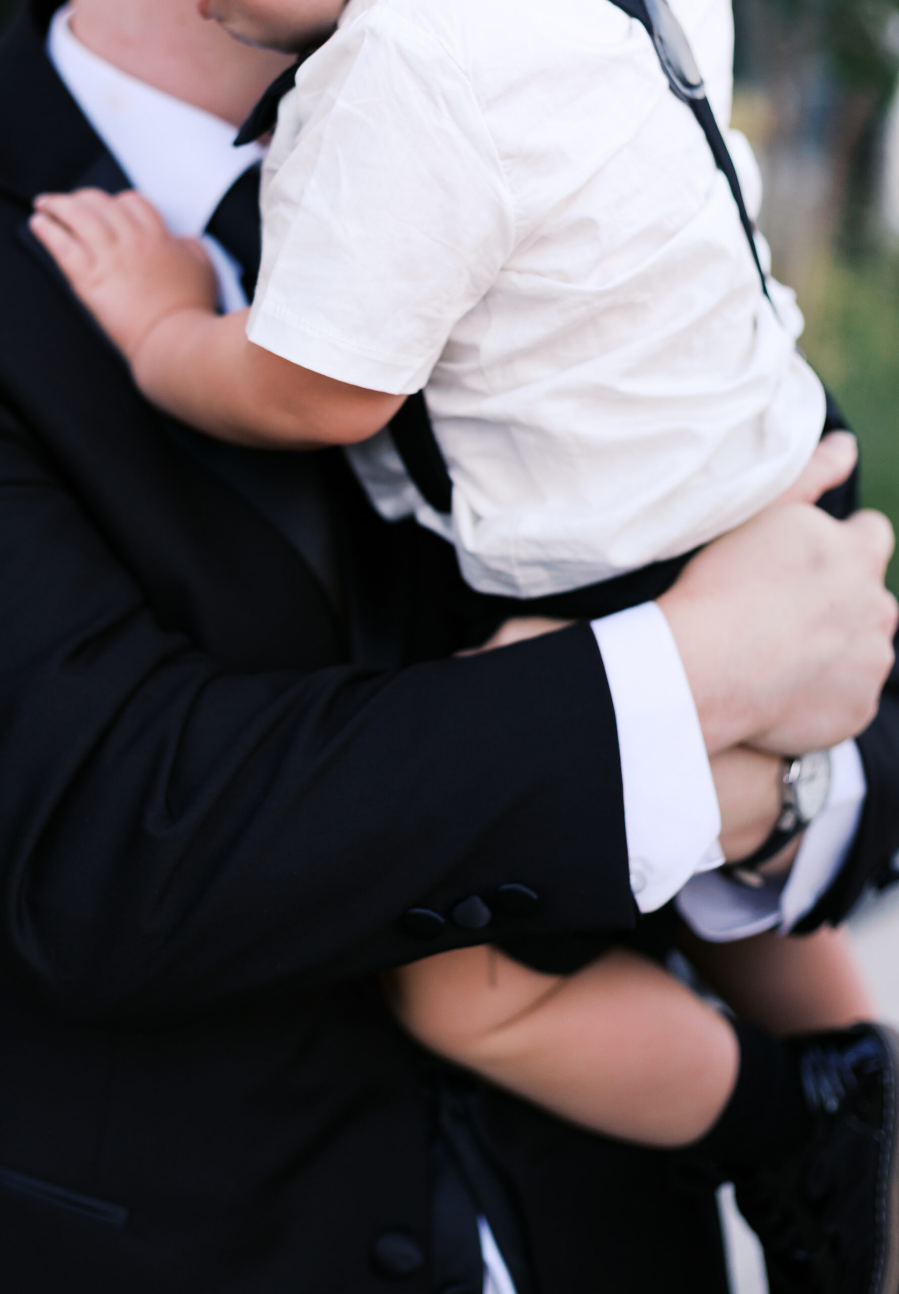 Close up detail shot of groom holding toddler dressed in formalwear.