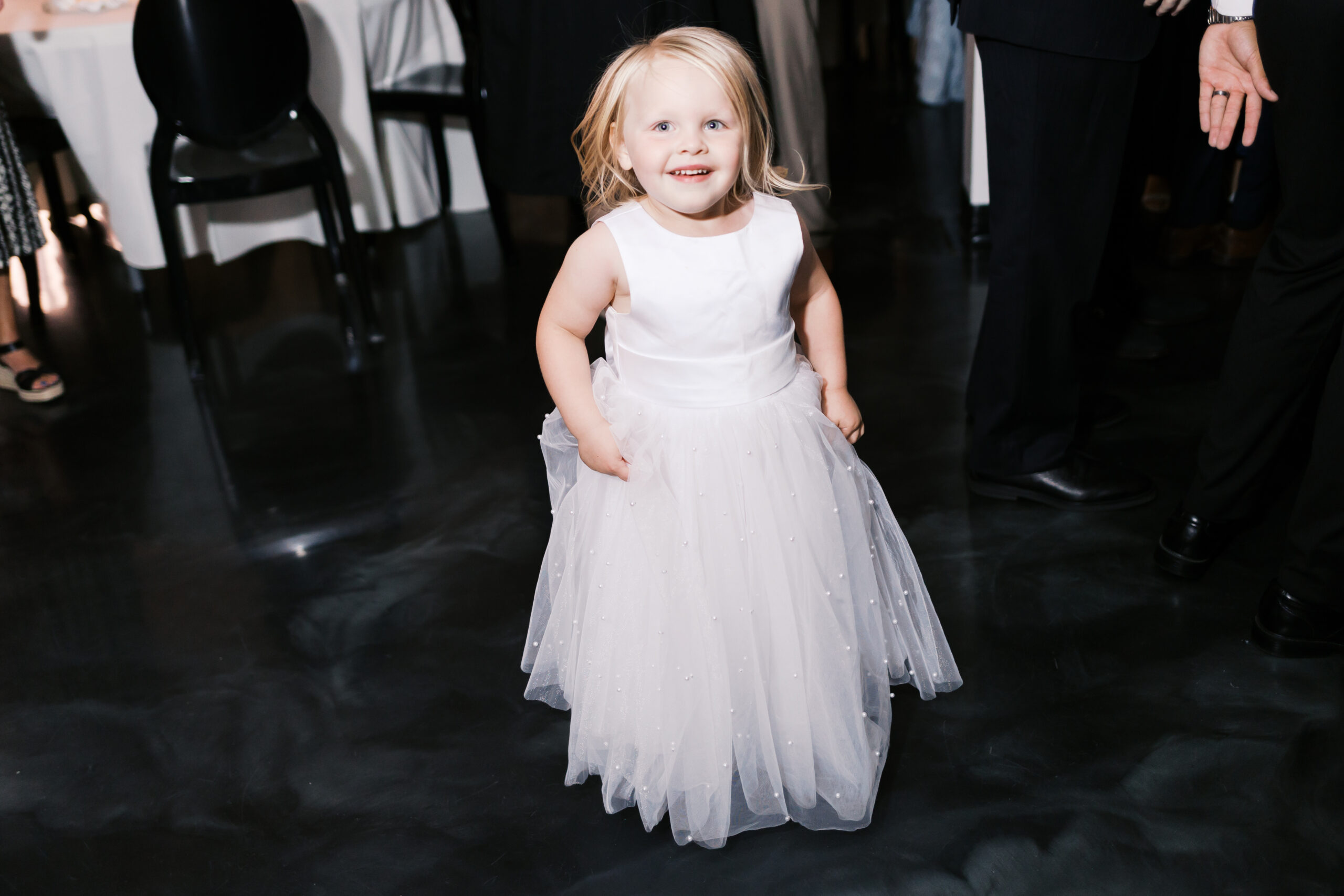 Toddler girl in a white dress dancing.