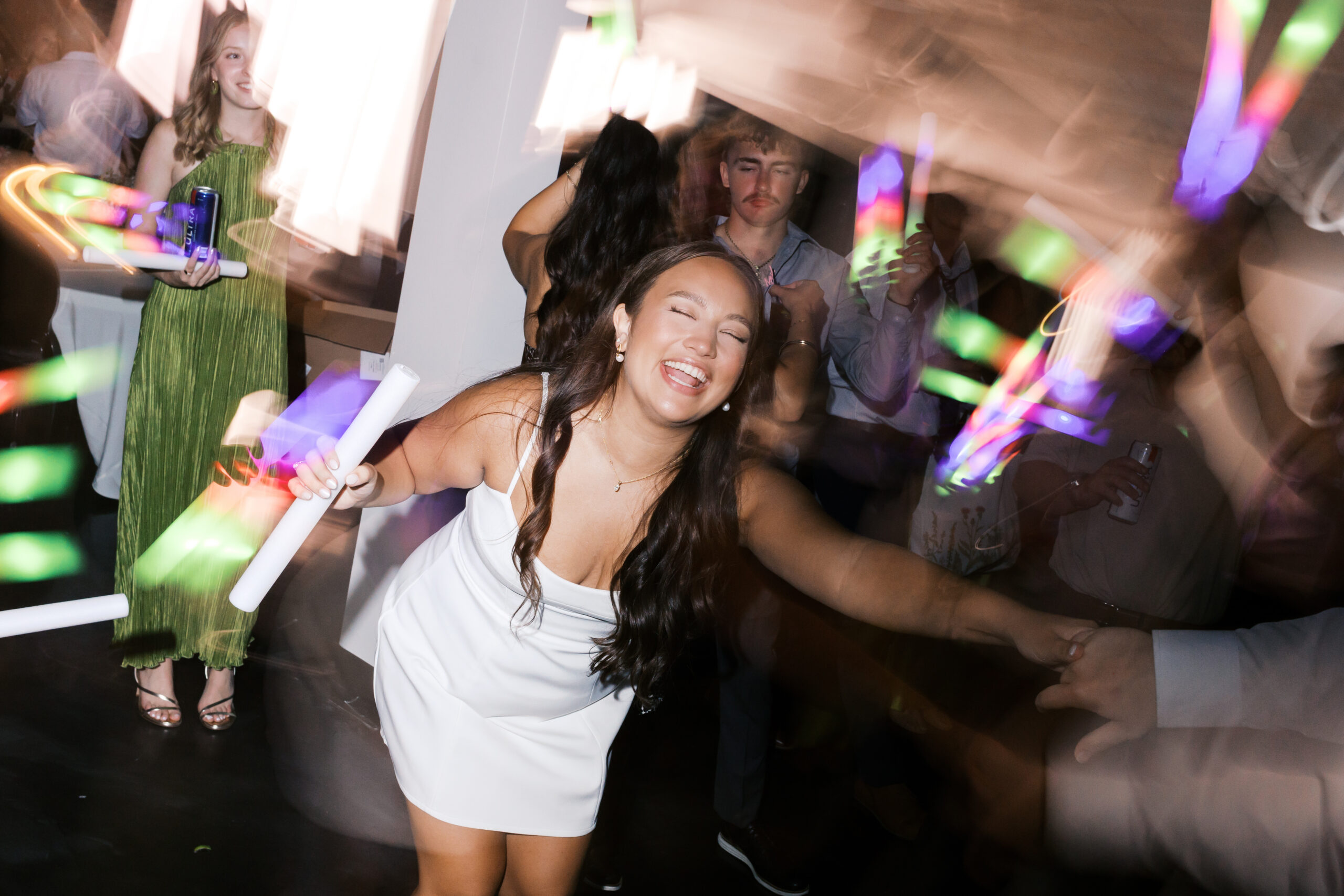 The bride smiling and laughing on the dance floor holding a light stick.