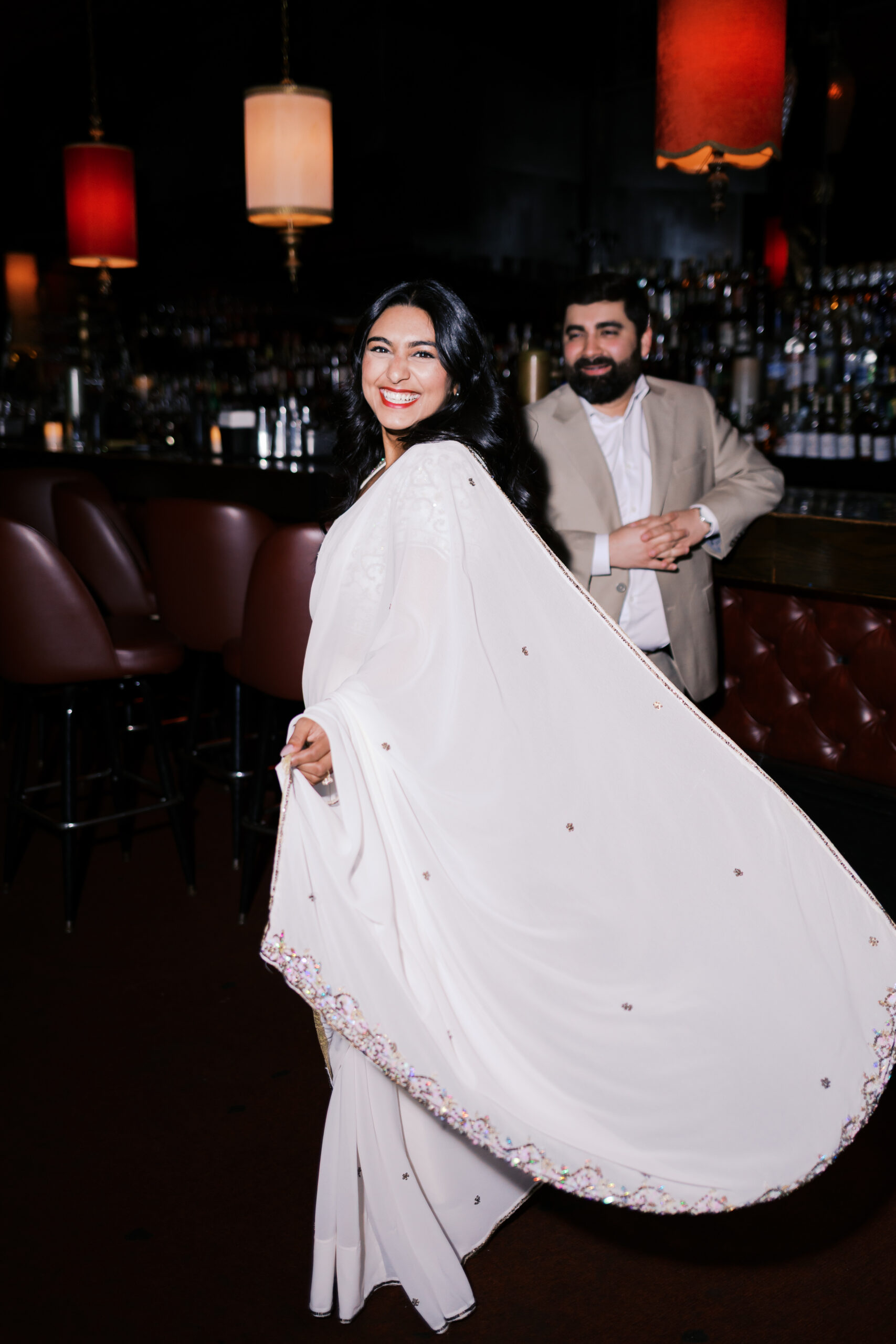 Bride-to-be twirling in a white saree with gold embroidery during a moody engagement session inside Green Lady Lounge in Kansas City.