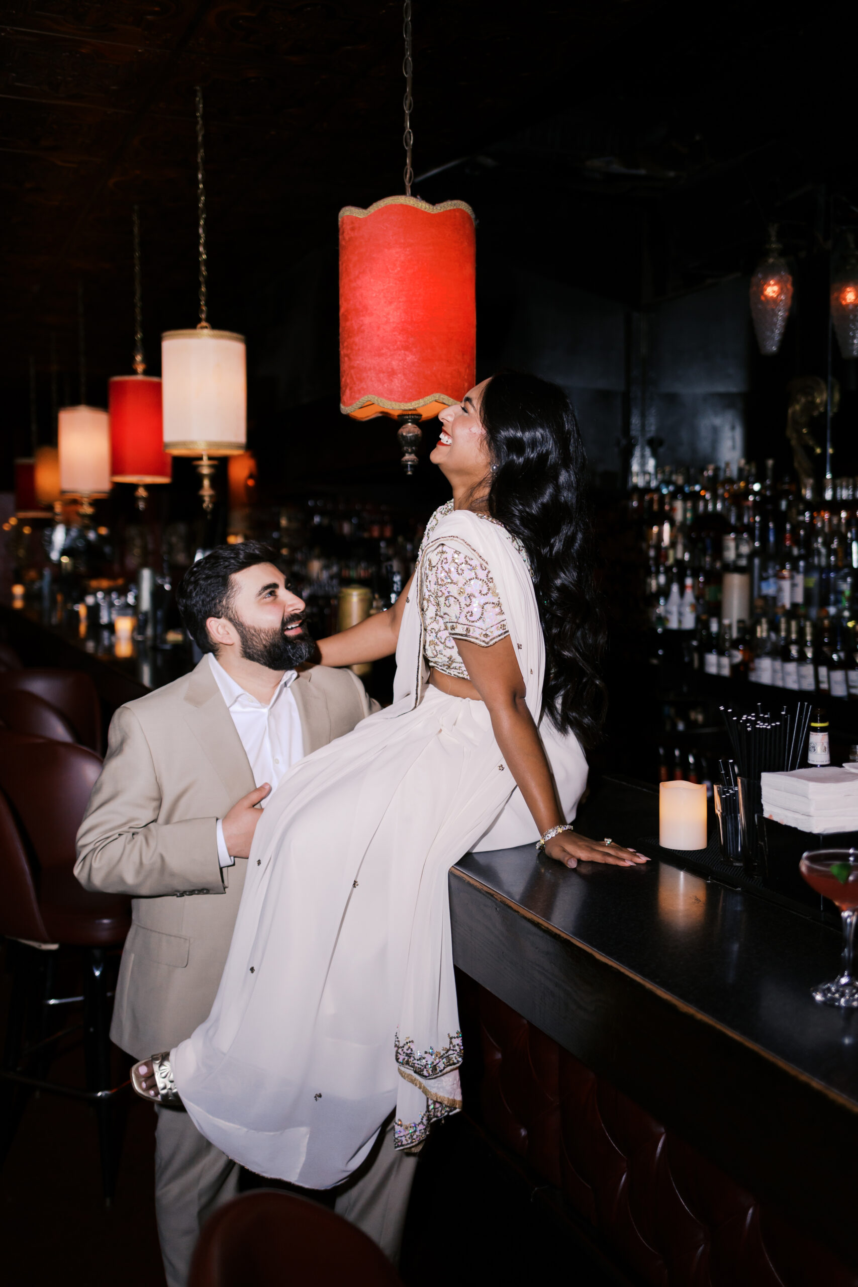 Man lifting his fiancée onto the bar during a playful engagement session at Green Lady Lounge in Kansas City.