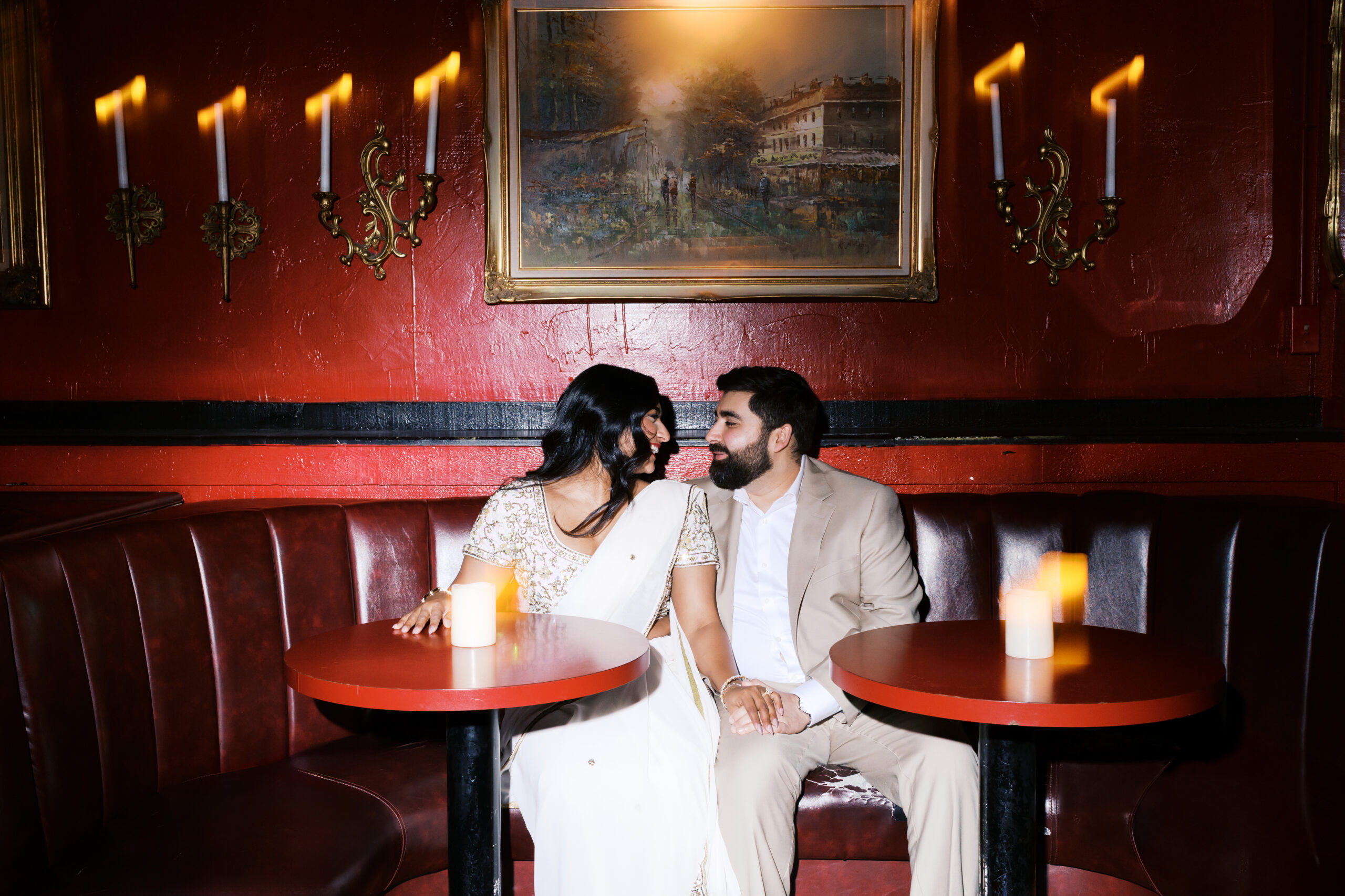 Engaged couple seated in a red leather booth at Green Lady Lounge in Kansas City, sharing an intimate moment beneath vintage wall sconces.