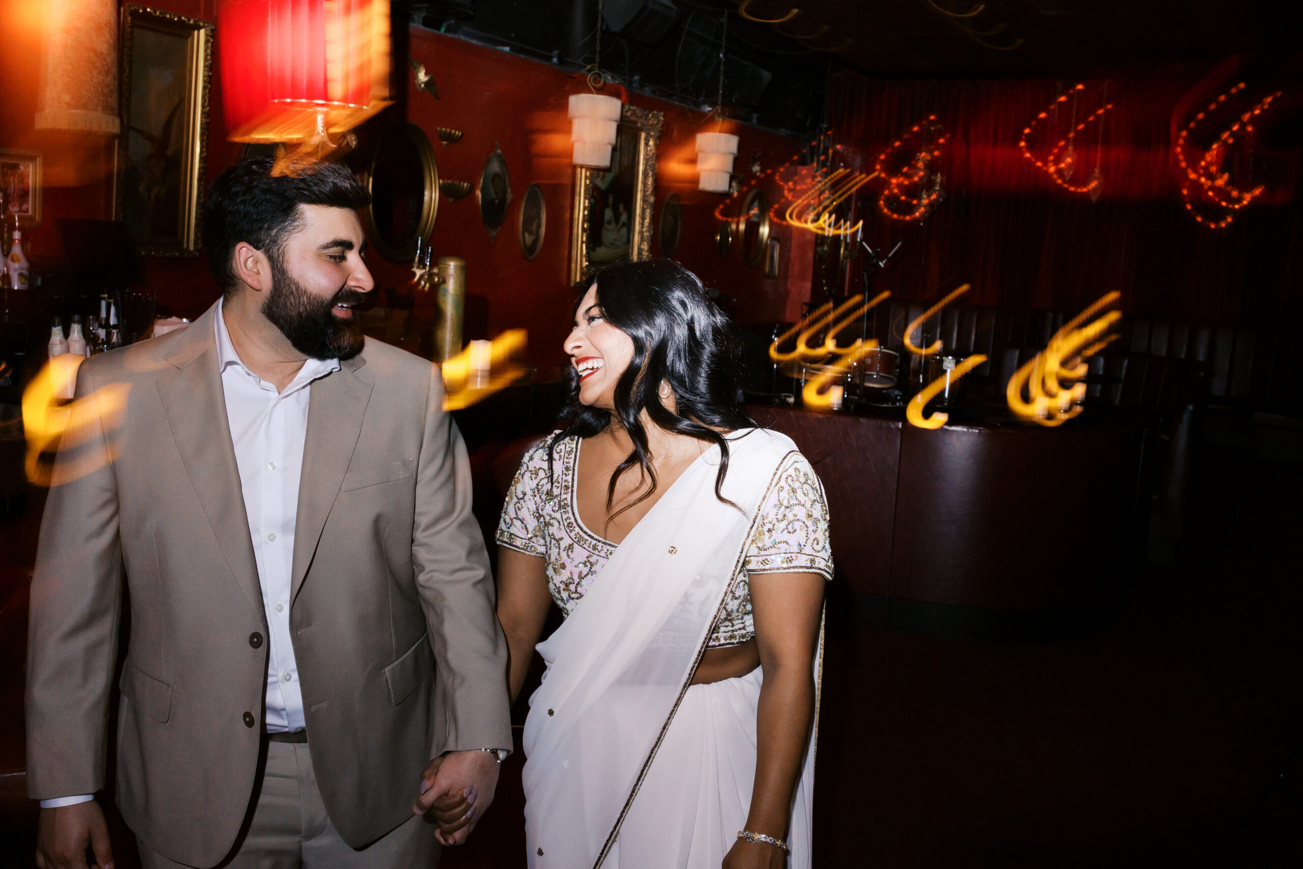 Couple holding hands and laughing inside Green Lady Lounge in Kansas City with warm light trails creating a cinematic engagement photo.