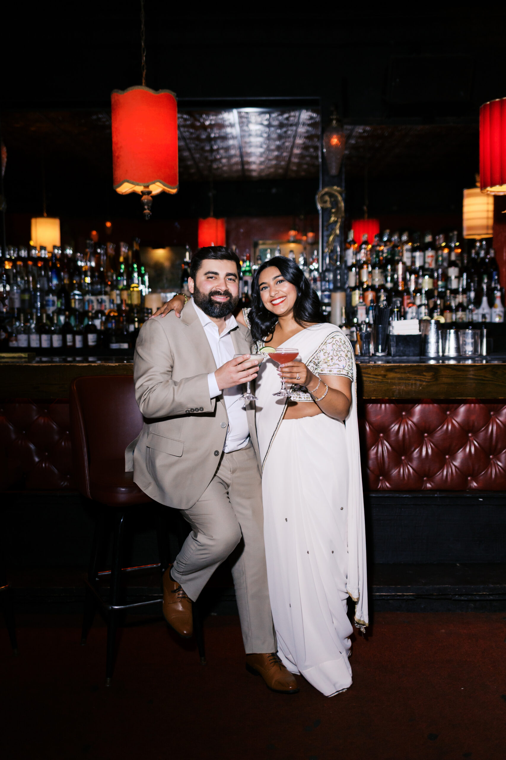 Engagement portrait of couple holding cocktails and smiling at the camera inside Green Lady Lounge in Kansas City.