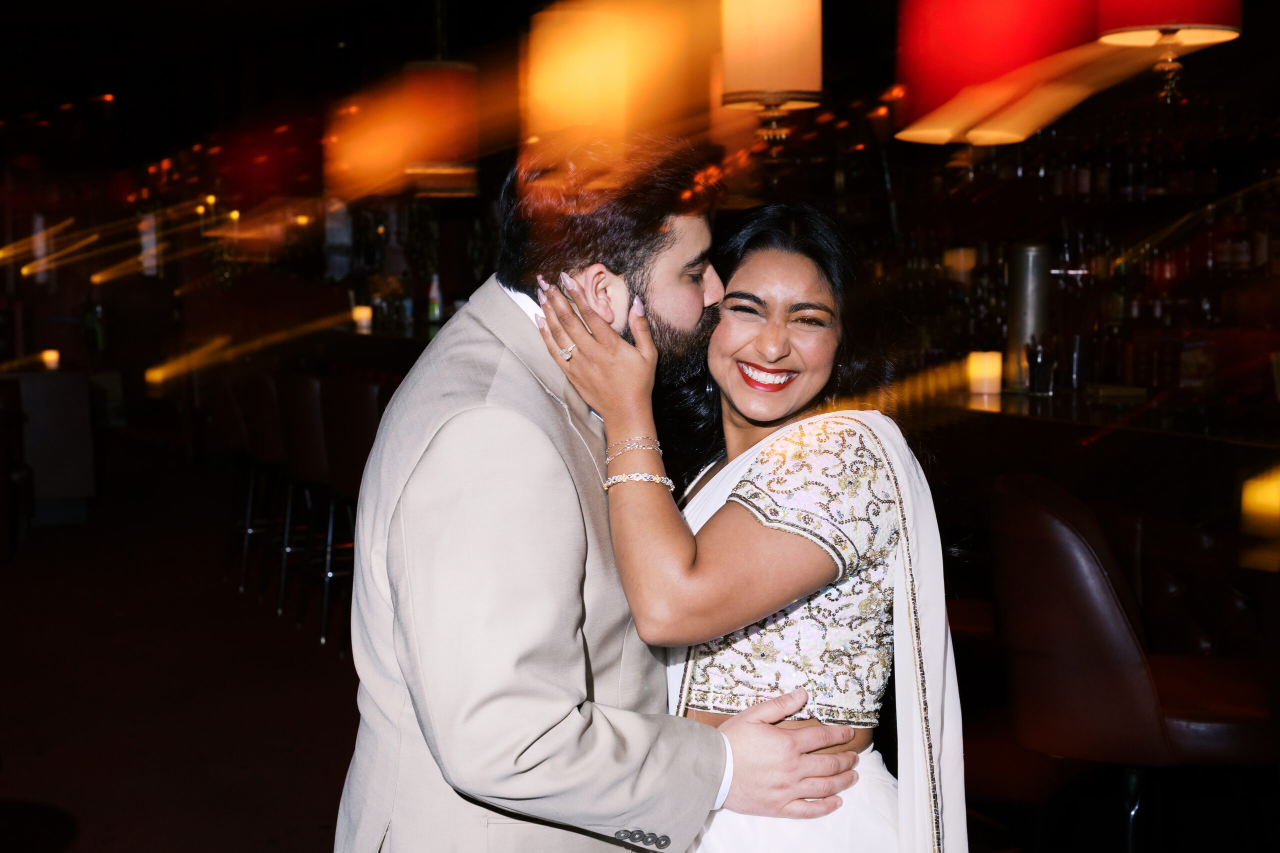 Editorial engagement photo of couple embracing in a dimly lit Kansas City jazz lounge with warm flash and romantic light flares.