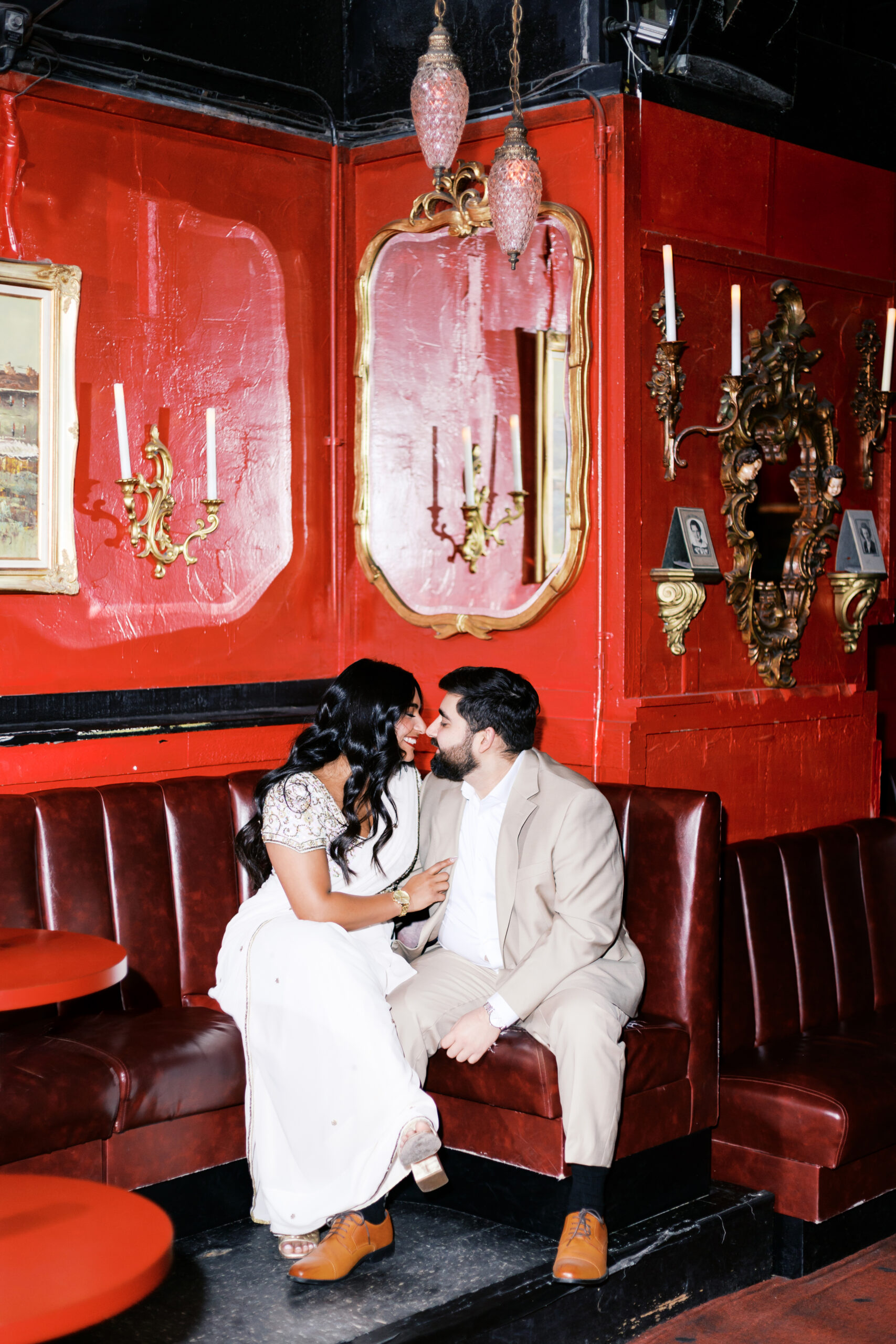 Couple sitting in a red leather booth at Green Lady Lounge in Kansas City, sharing an intimate moment during their moody bar engagement photo session.